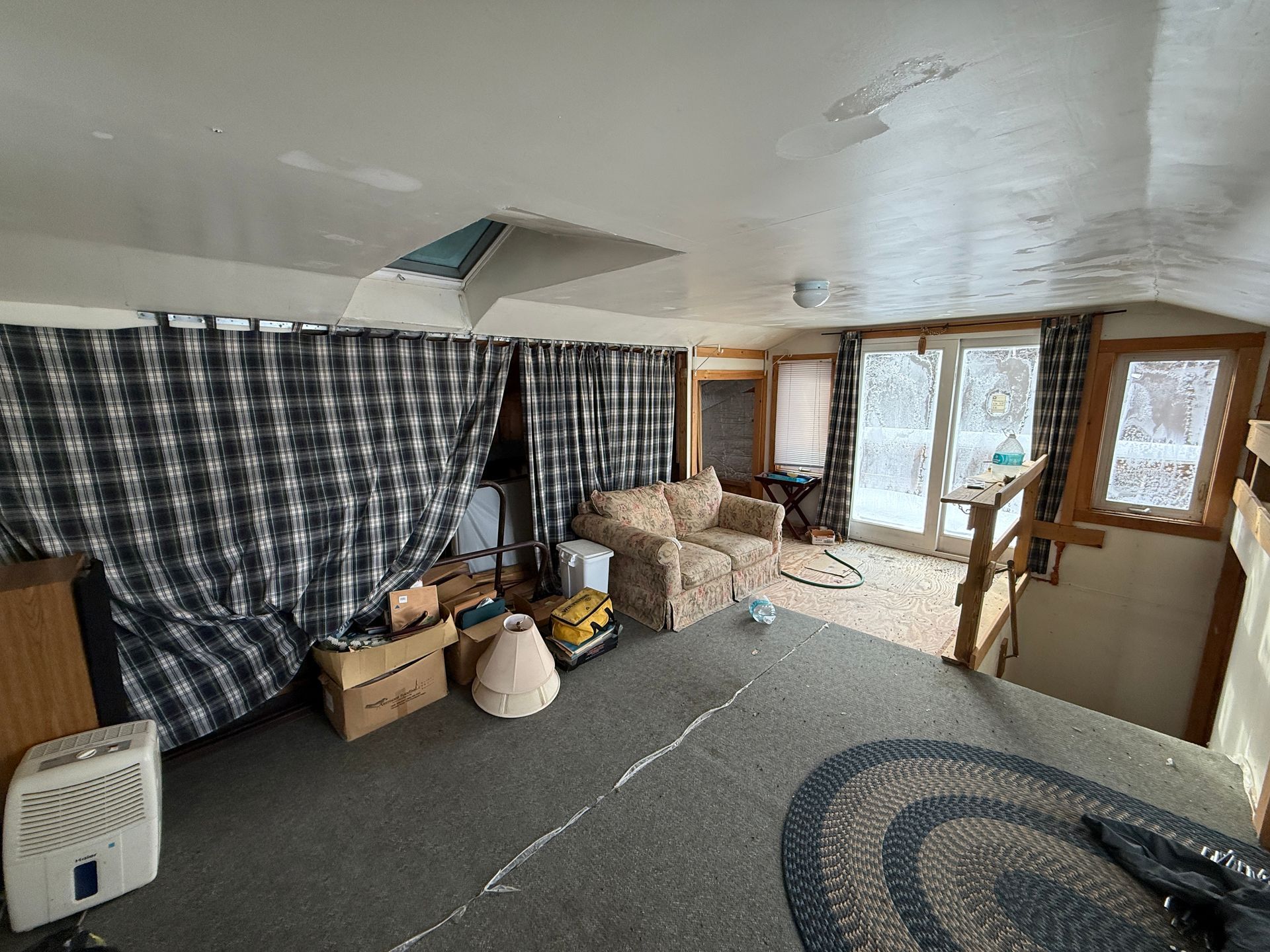 Interior room with gray carpet, plaid curtains, and a couch. Windows overlook a snowy scene.