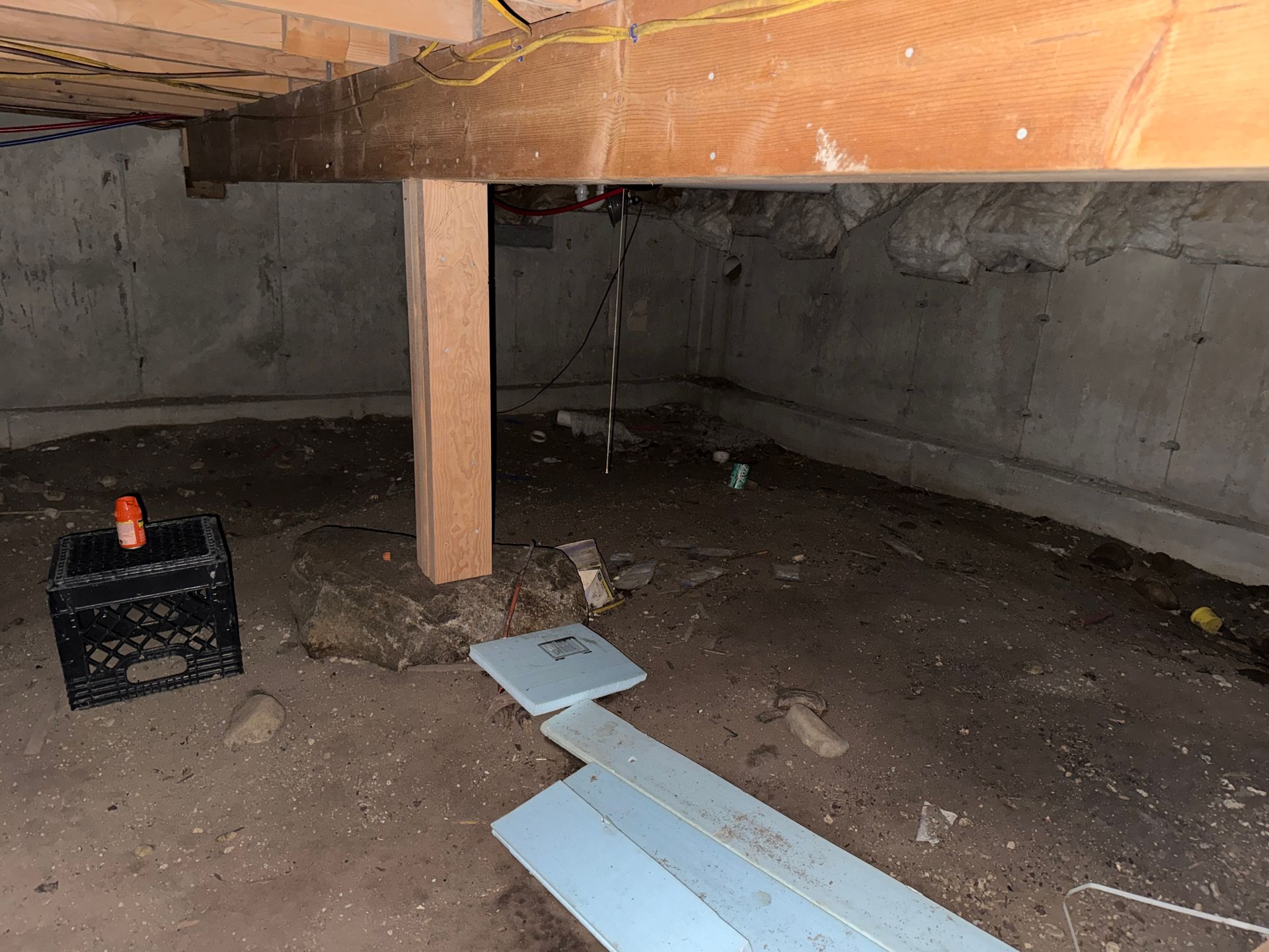 Under-house crawl space: dirt floor, concrete walls, wooden beams, support post, plastic crate.