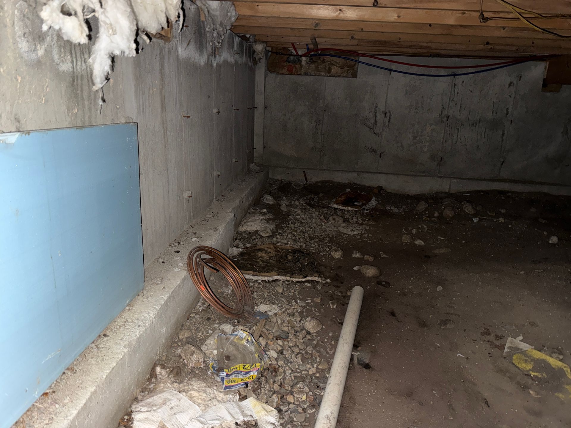 Basement corner with concrete walls, exposed wood, and a blue wall patch.