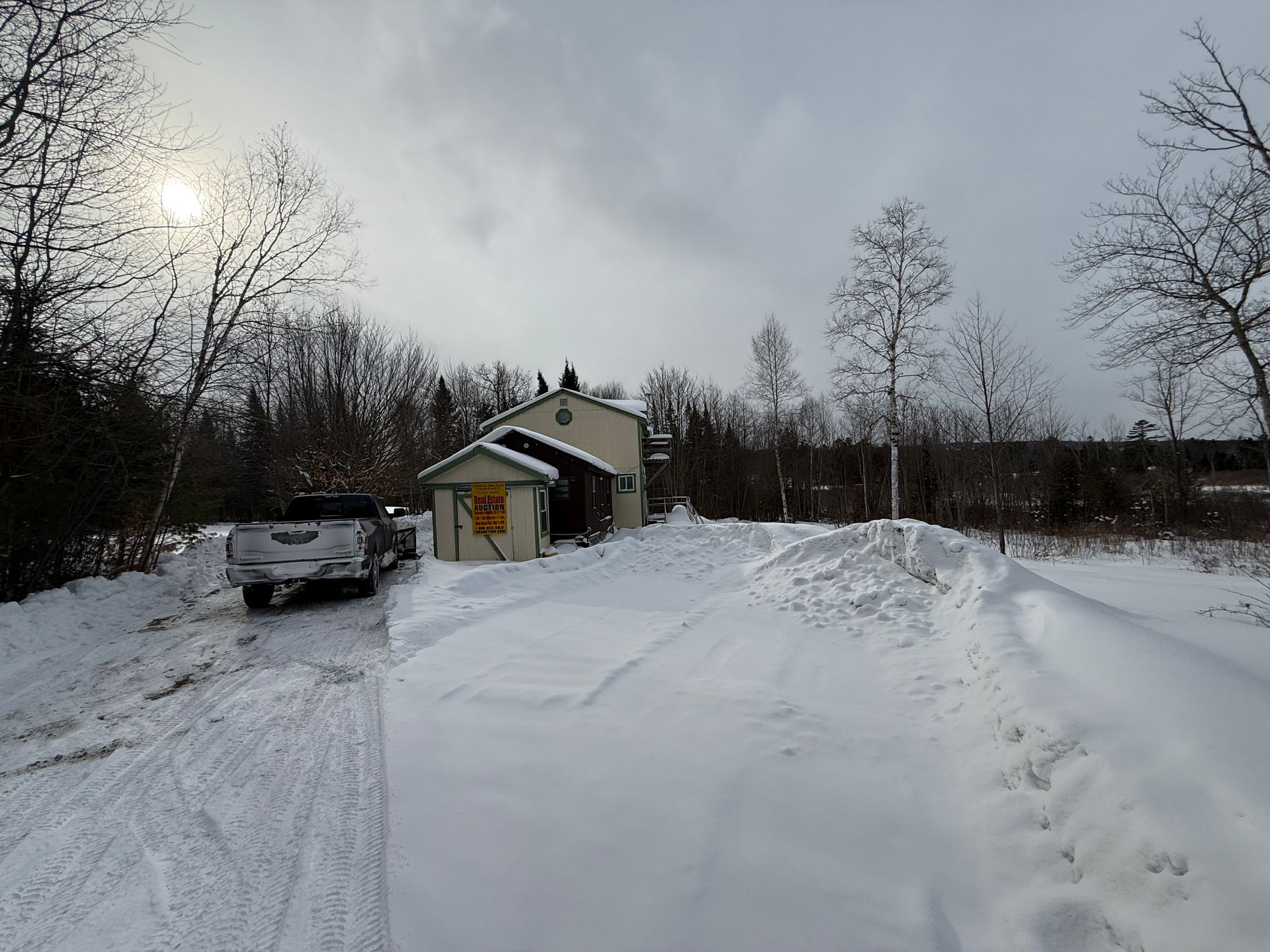 Snow-covered house with a pickup truck in the snowy driveway, set against a cloudy sky.