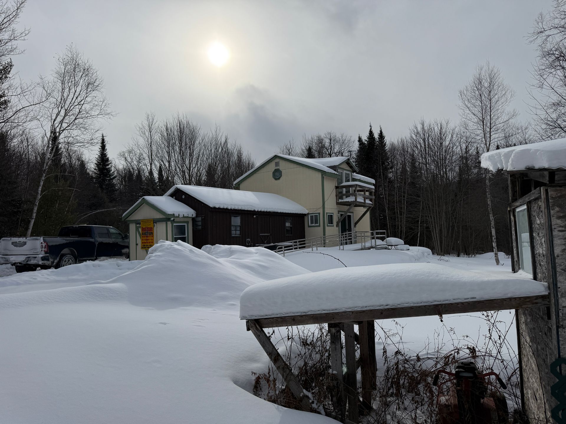 Snowy landscape with a house and outbuilding, bright sun peeking through clouds.