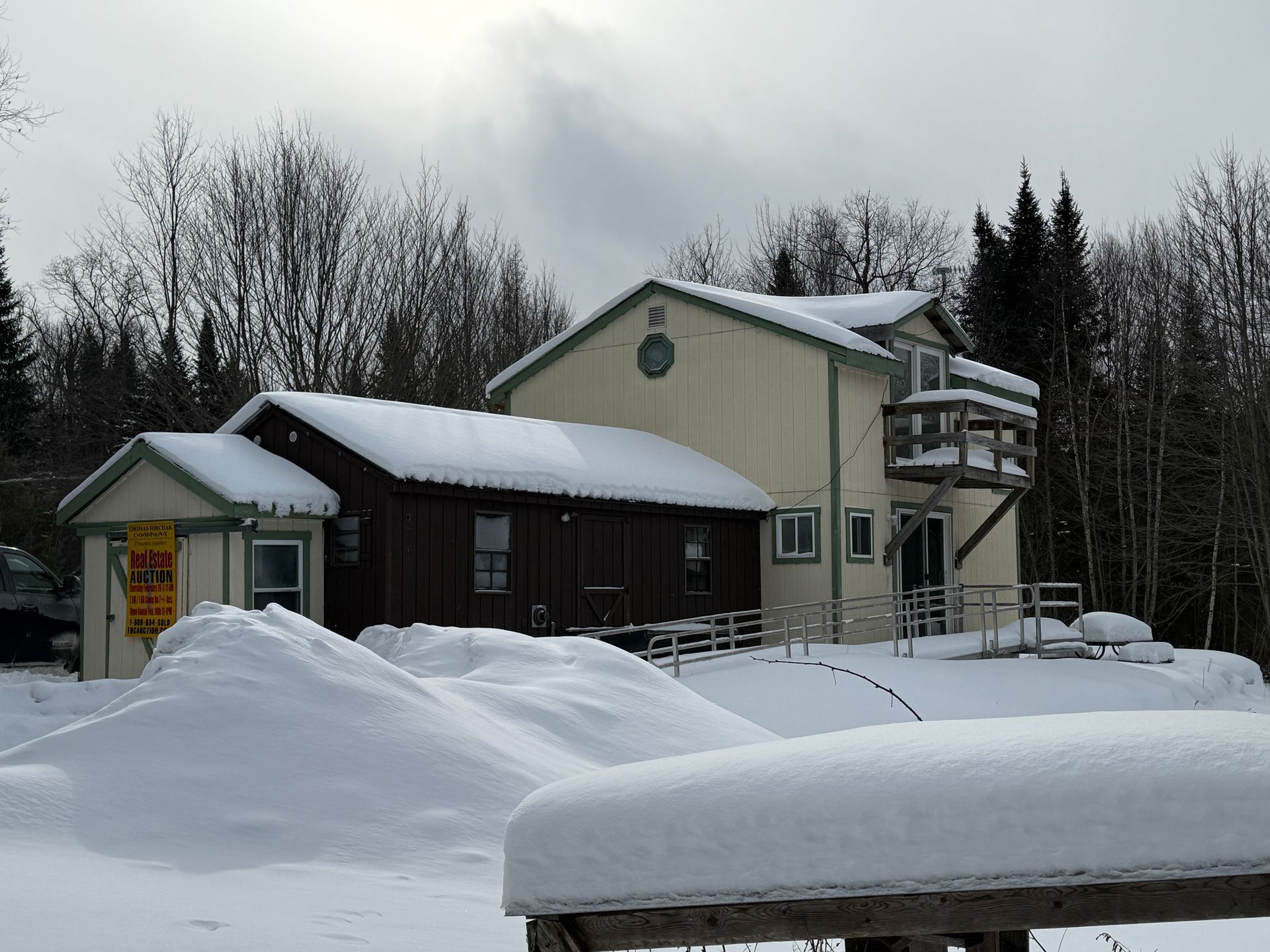 Snowy multi-building structure with ramp and deck, against a forest under a cloudy sky.