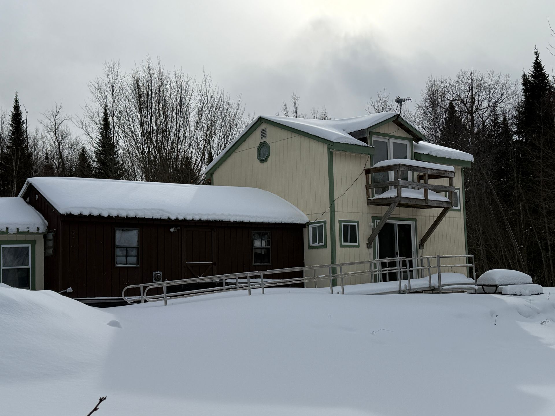 A two-story building in a snowy setting with a wheelchair ramp. Light-colored walls, brown roof, and deck.