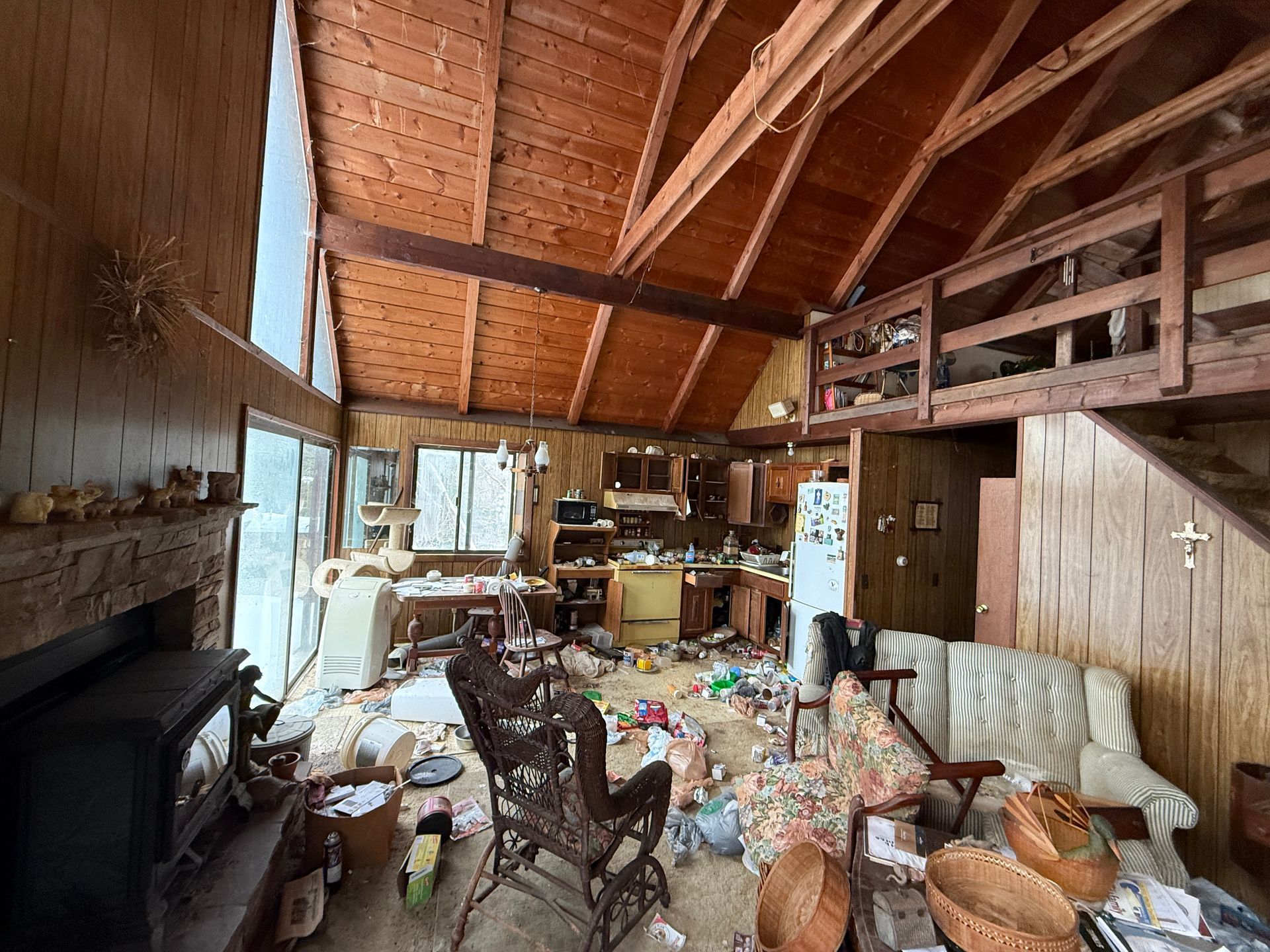 Interior of a wooden cabin with open layout; fireplace, kitchen, and loft are visible.