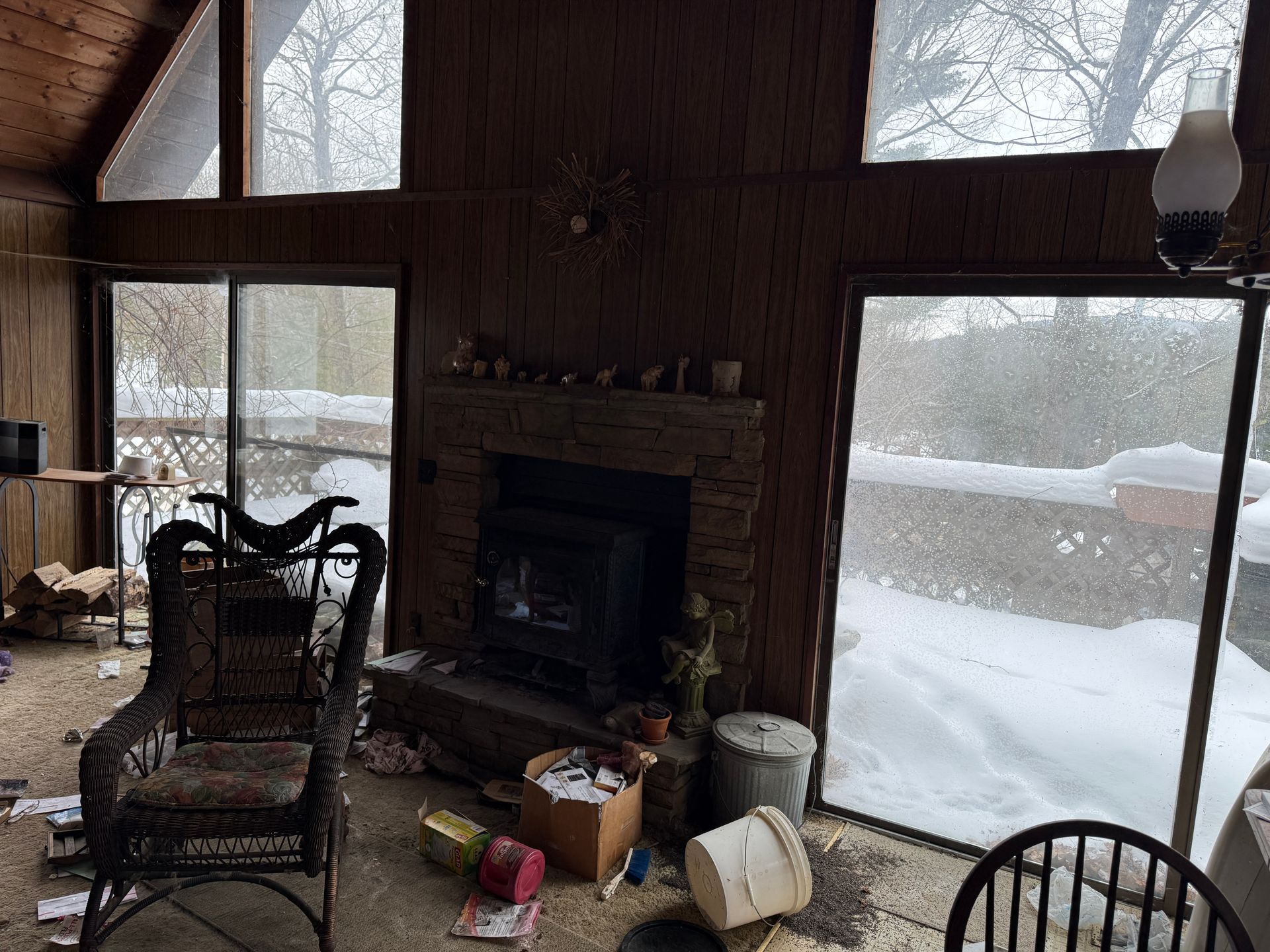 Interior of a snow-covered sunroom with a fireplace, wicker chair, and sliding glass doors.