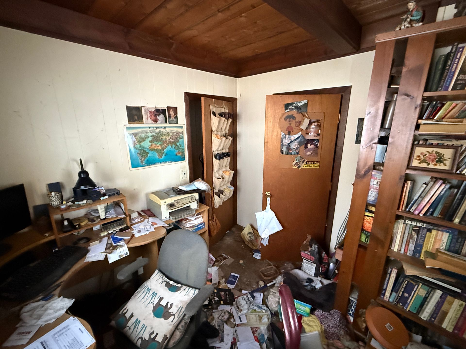 Room with desk, chair, shelves, and wood-paneled ceiling.