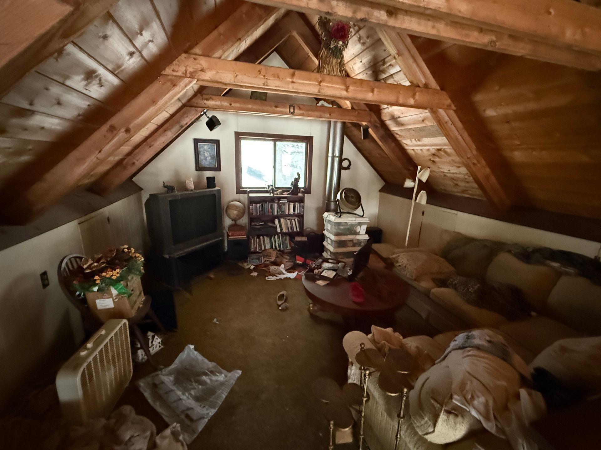 Attic room with a TV, couch, books. Window in the back. Wooden beams visible.