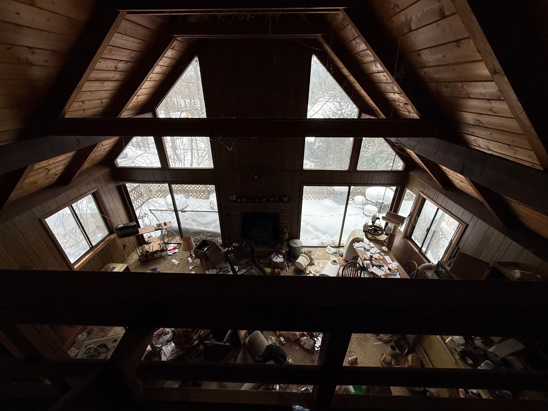 Interior view from above of a living room with large windows and a fireplace.
