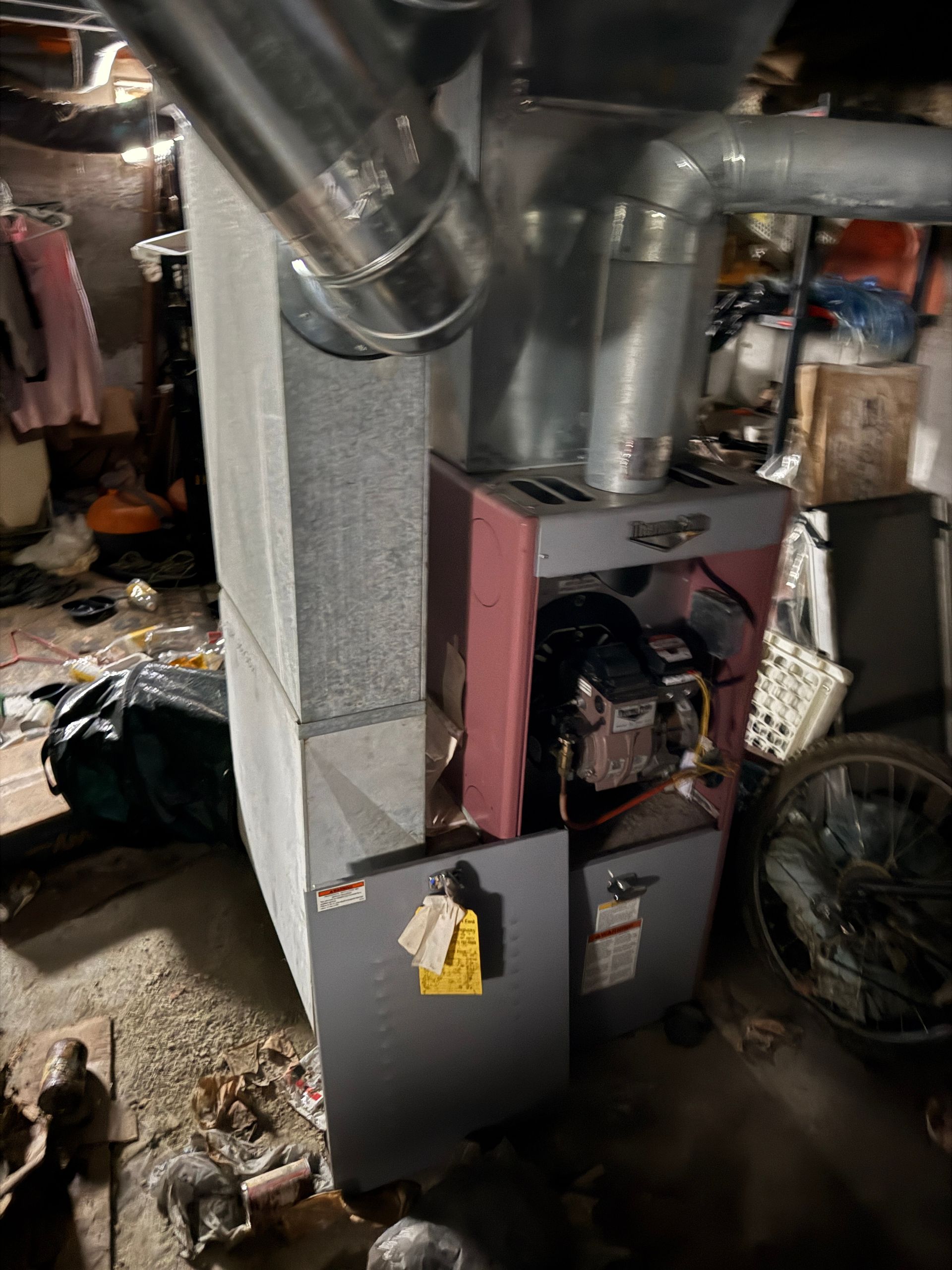 Furnace with metal ductwork in a basement setting. Gray and red.