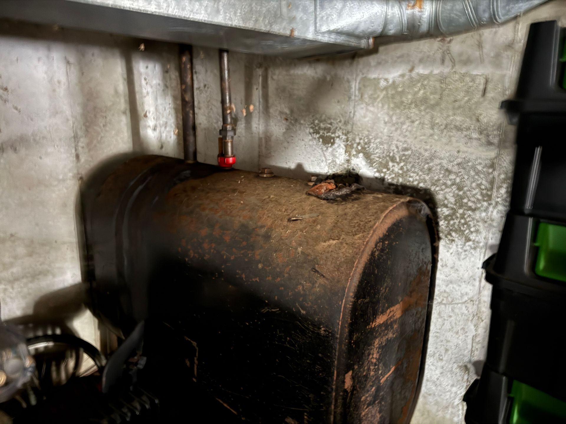 Oil tank in a basement corner with pipes above and storage bin to the right.