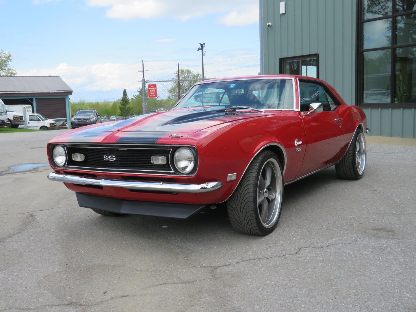 Red classic Chevrolet Camaro parked near a building on a sunny day.