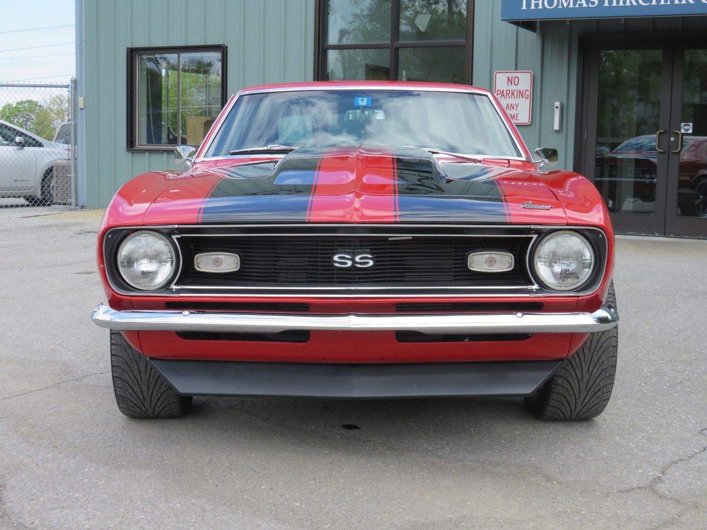 Red 1967 Chevrolet Camaro SS with black racing stripes parked in front of a building.