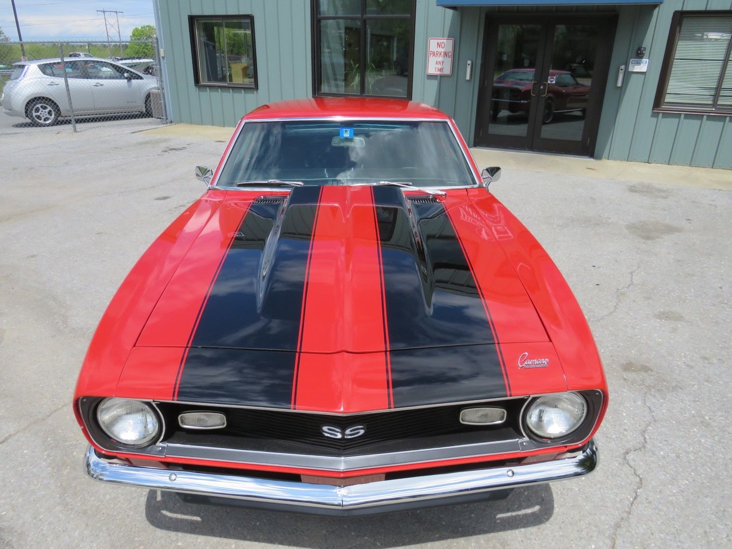 Red classic car with black racing stripes parked outside a building.