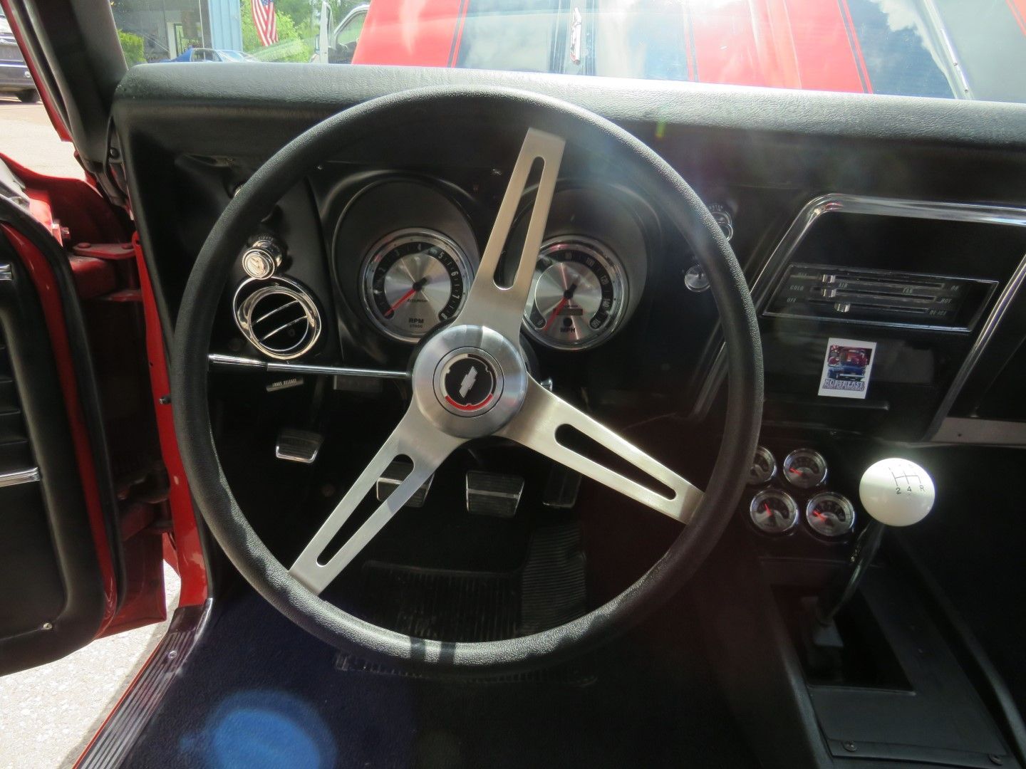 Interior of a red classic car, showing a steering wheel, gauges, and a white shift knob.
