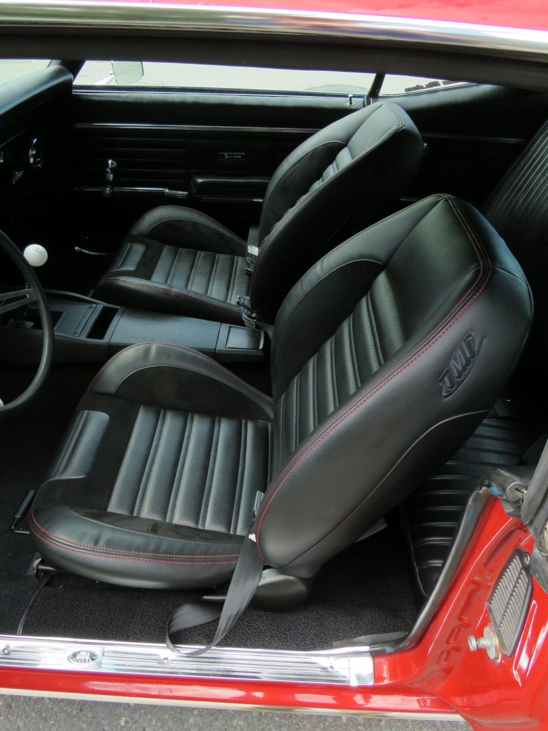Black car seats with red stitching inside a red classic car.