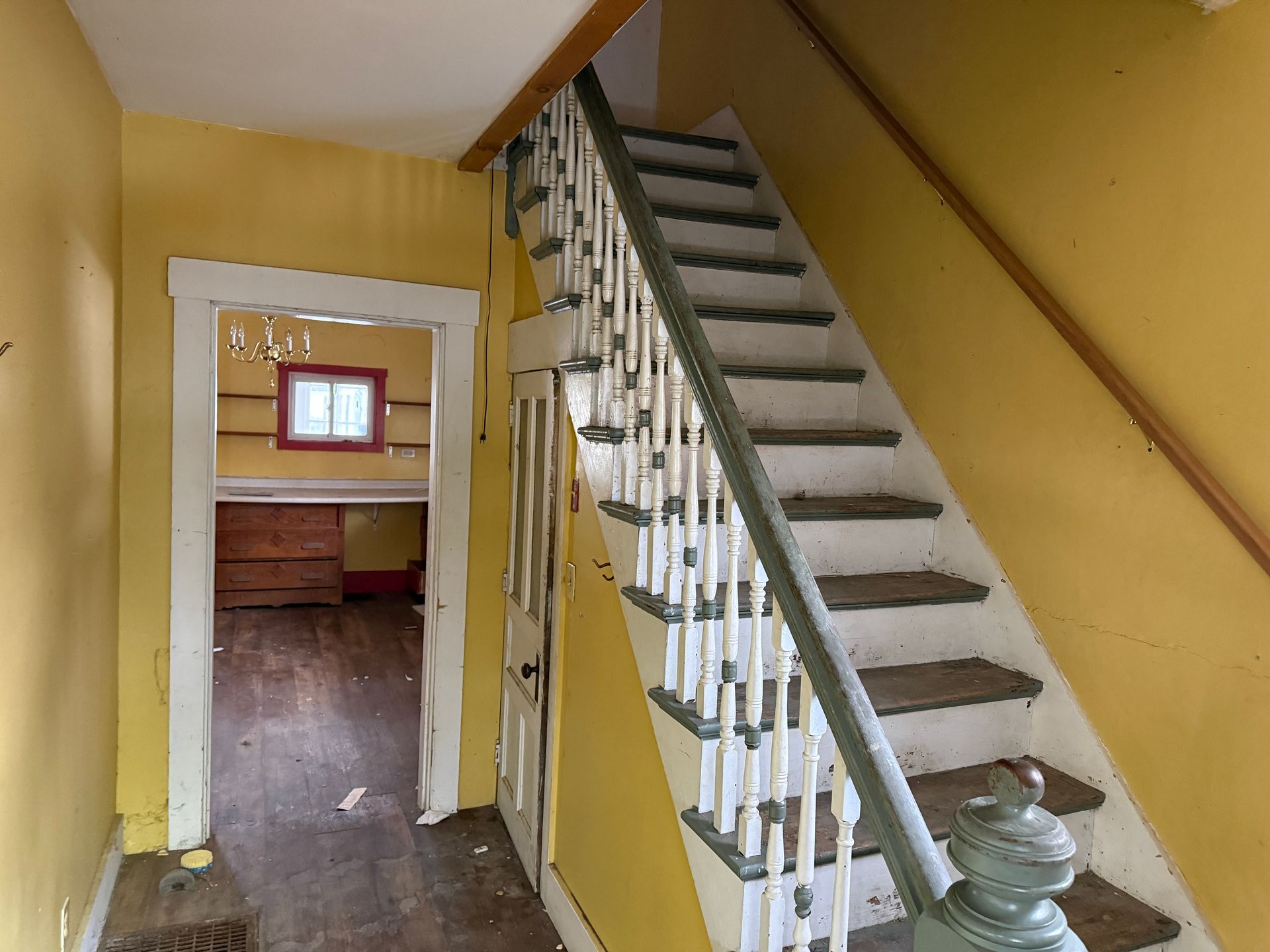 A yellow entryway with a wooden staircase and a doorway leading to a room with a window.