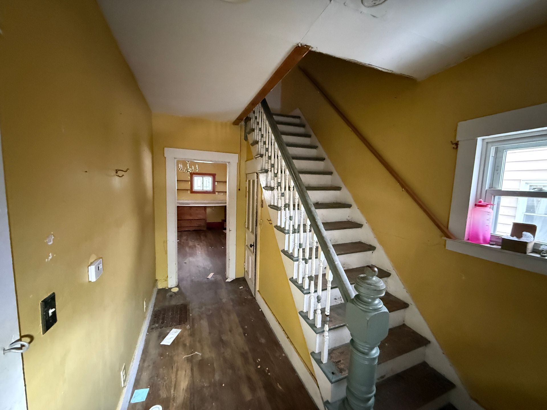 A hallway with mustard-yellow walls, wood floors, and an uncarpeted staircase with white railings.