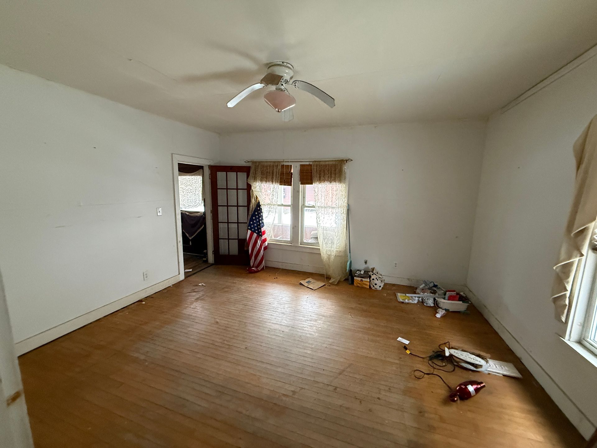 An empty room with light wood floors, white walls, a ceiling fan, and a window.