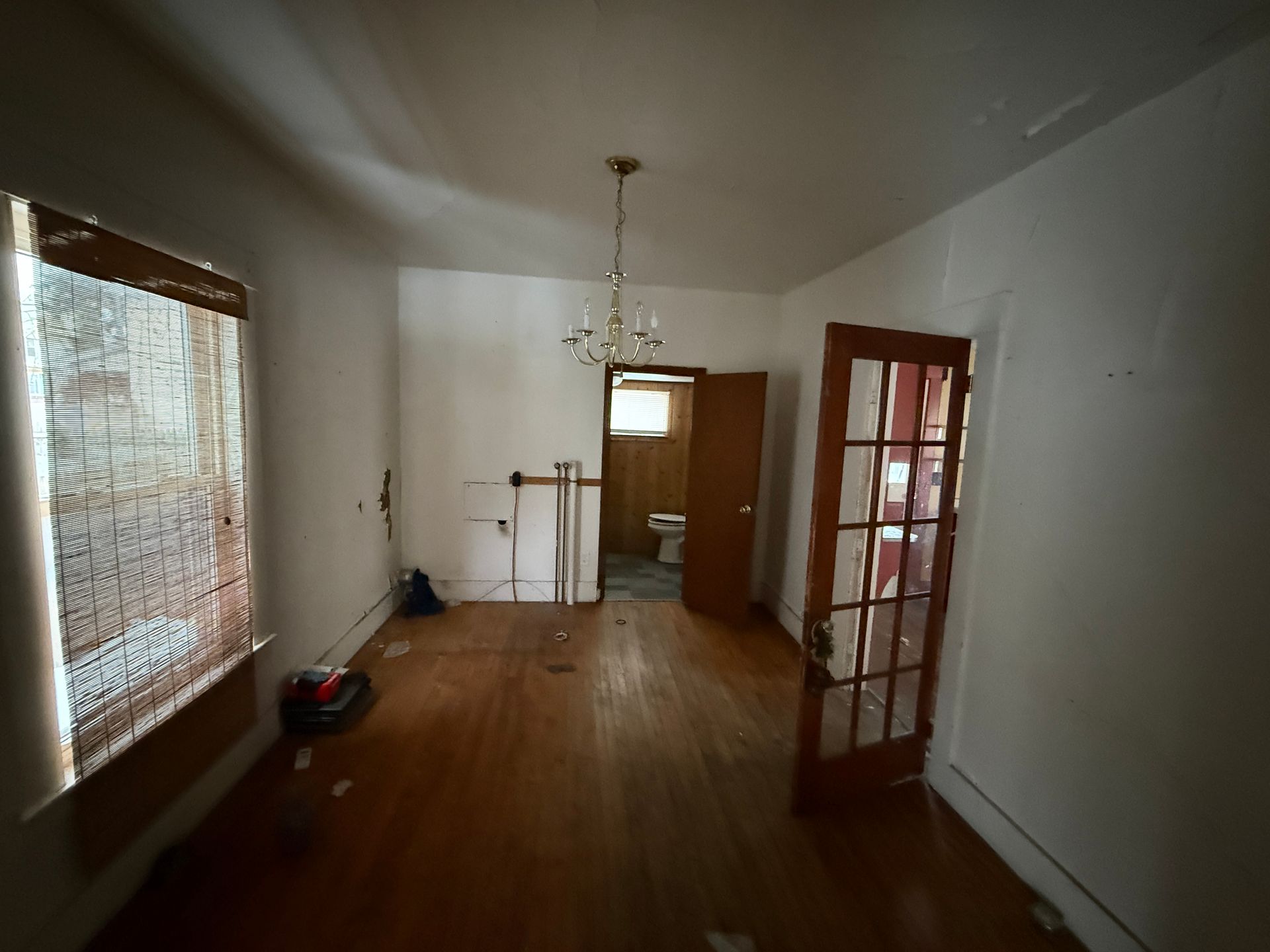 An interior view of a room with wood floors, white walls, a hanging light fixture, and an open glass-paneled wooden door.