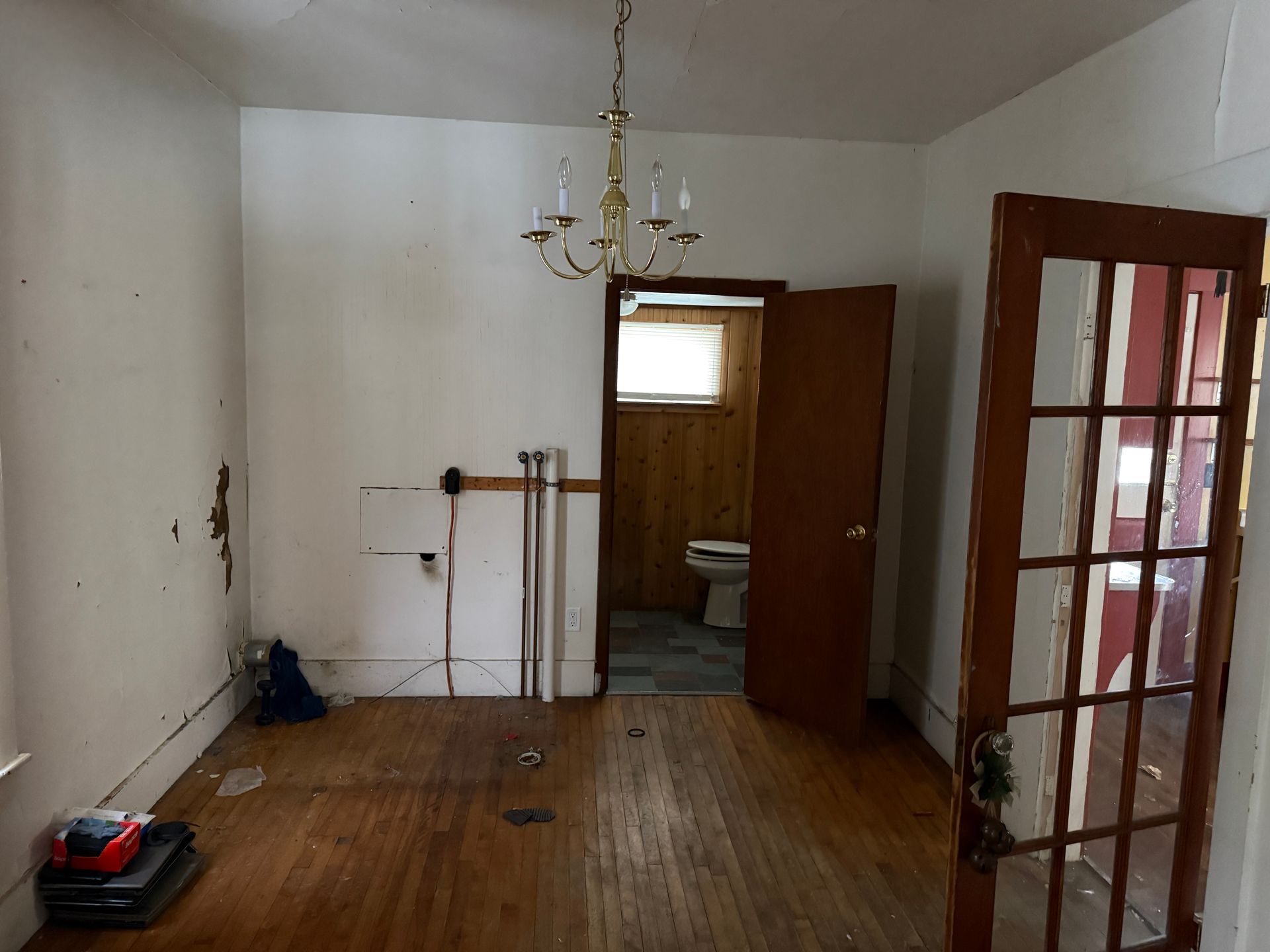 A room with wooden floors, a chandelier, and an open doorway leading to a bathroom.