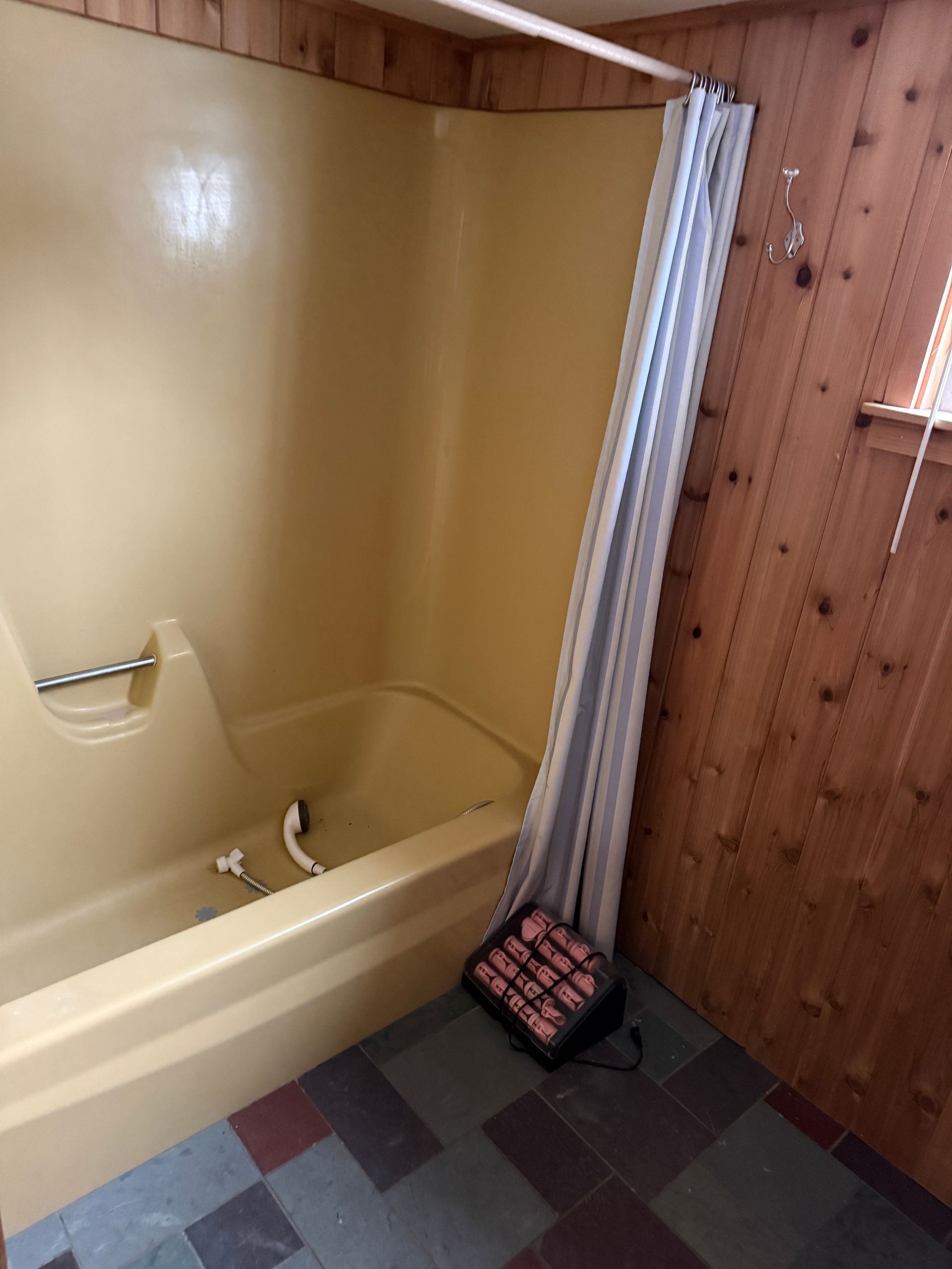 A beige bathtub with a shower curtain and a small electric space heater sitting on the floor beside it.