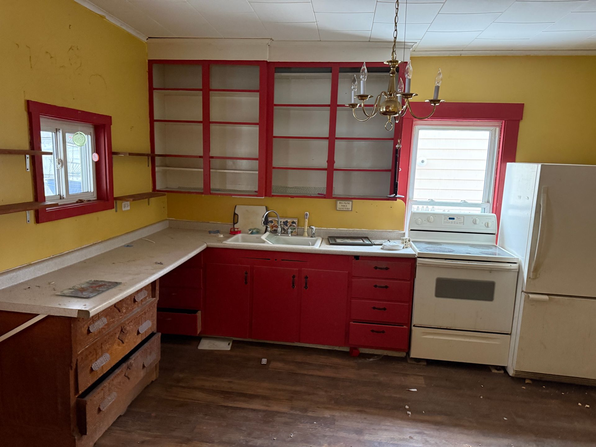 A kitchen with yellow walls, red cabinets, glass-front cupboards, a white stove, a white refrigerator, and wood flooring.