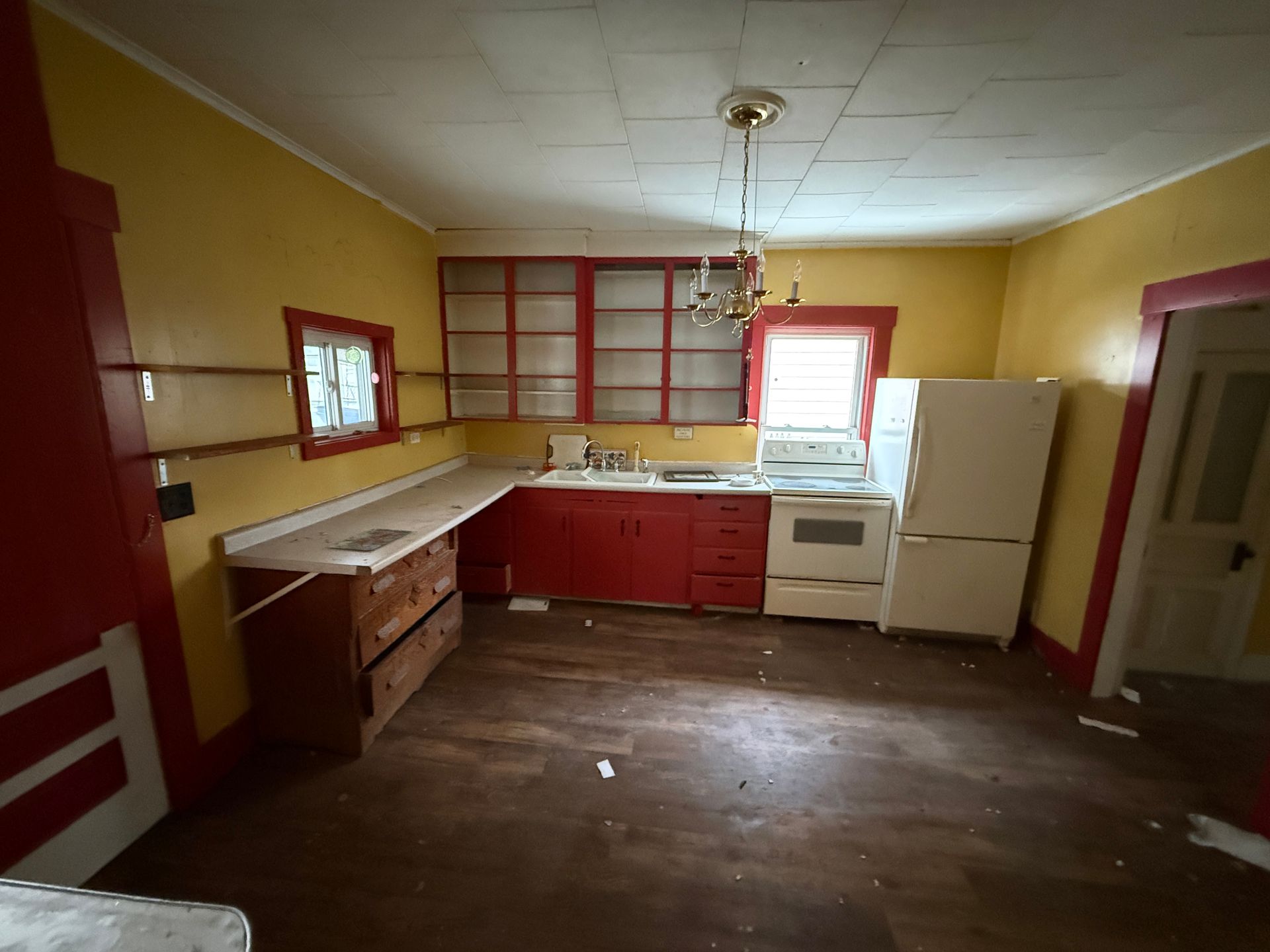 Kitchen with bright yellow walls, red cabinets and trim, wooden floors, a white stove, and a white refrigerator.