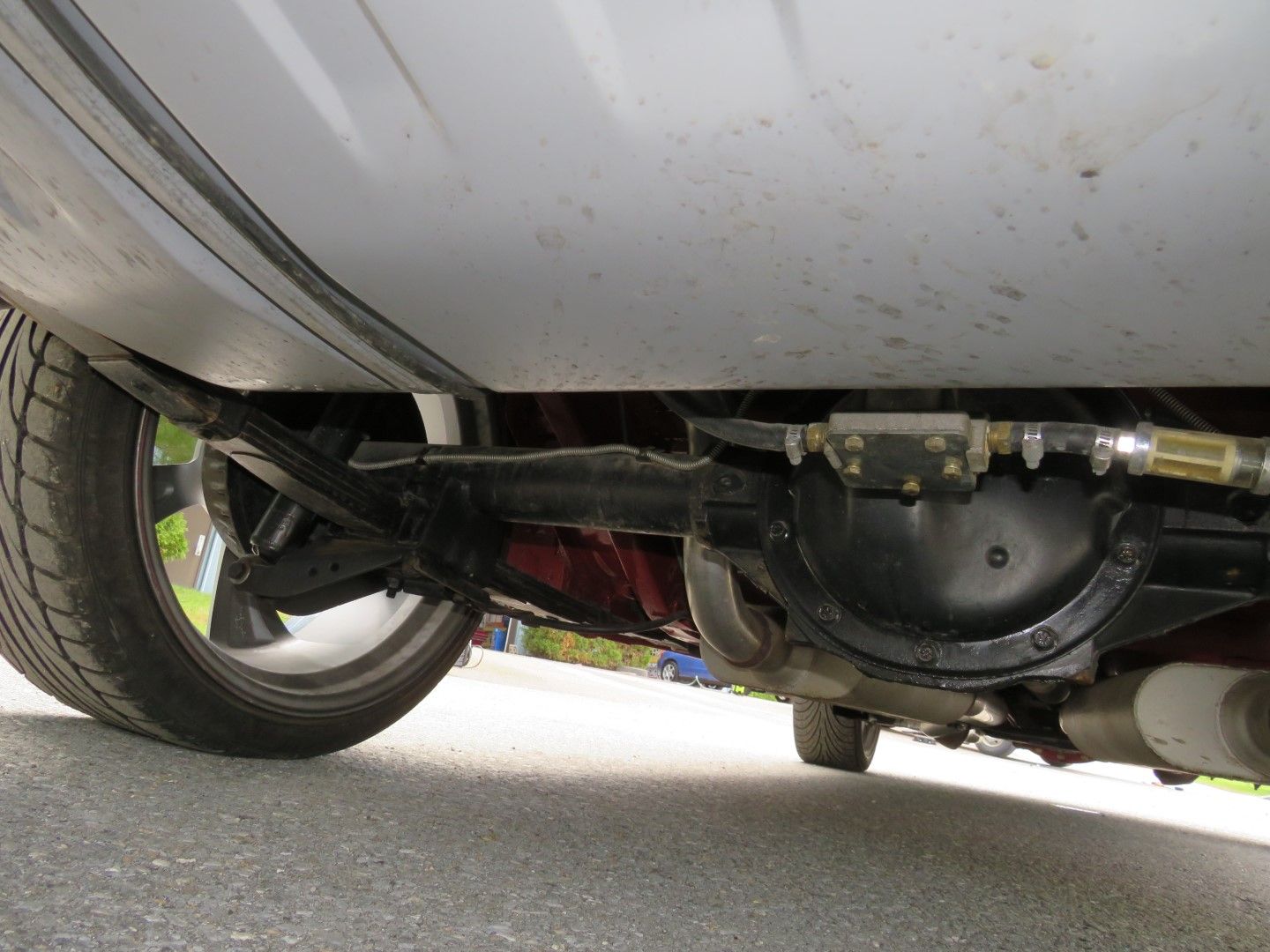 Underside view of a car's rear suspension, including the axle, tires, and exhaust.