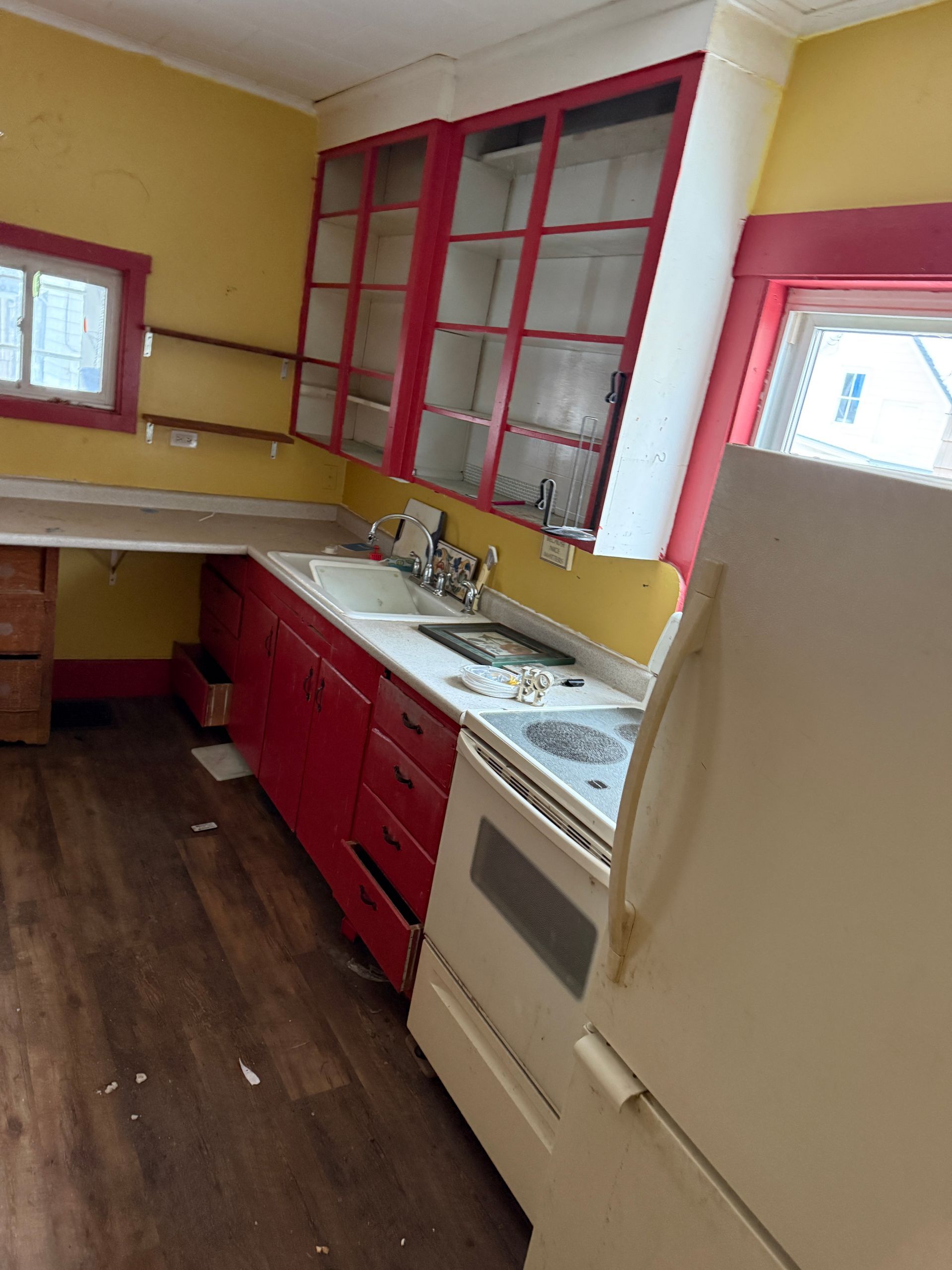 A kitchen with red cabinets, yellow walls, wood-look flooring, a white stove, and a white refrigerator.