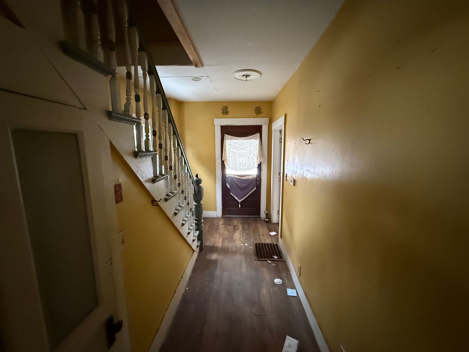 A yellow-walled hallway with a wooden staircase on the left, wood-look flooring, and a door at the end.