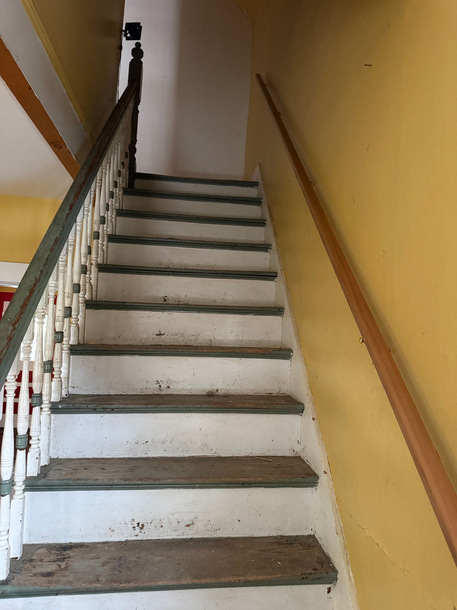 An indoor staircase with white risers and wooden treads, yellow walls, and a wooden handrail on the left and right.