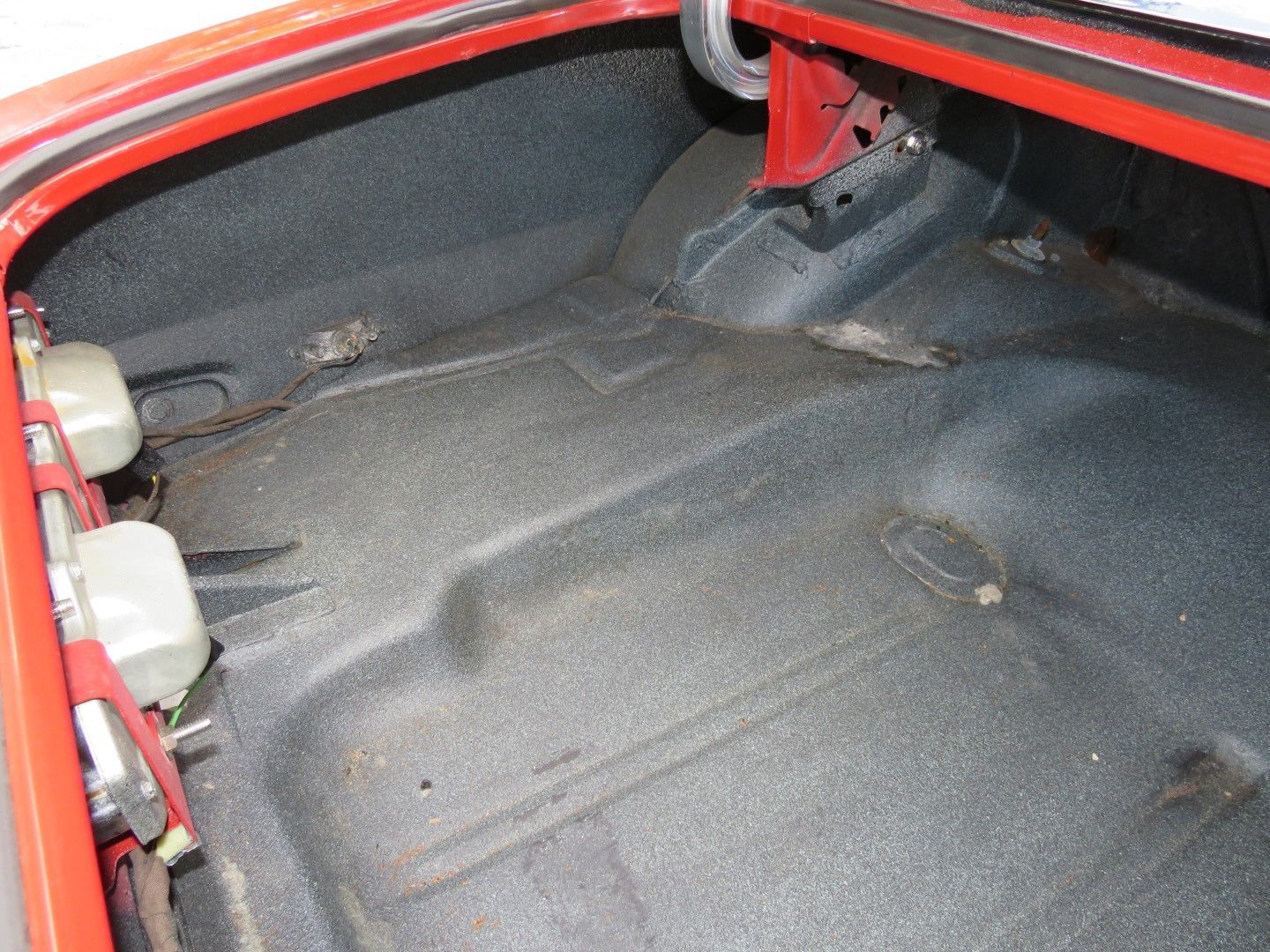 Empty, textured trunk of a red car, showing floor, side panels and tire well.
