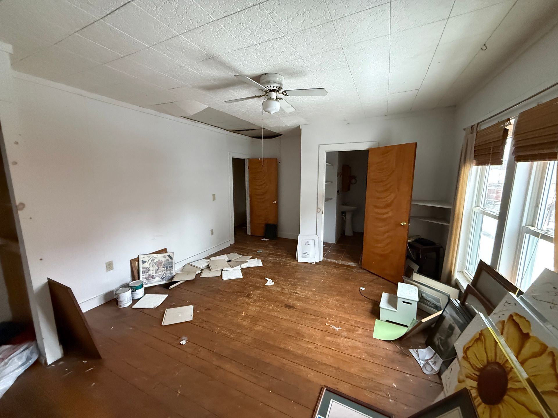 A room with wooden floors, white walls, a ceiling fan and two open doorways leading to other rooms.