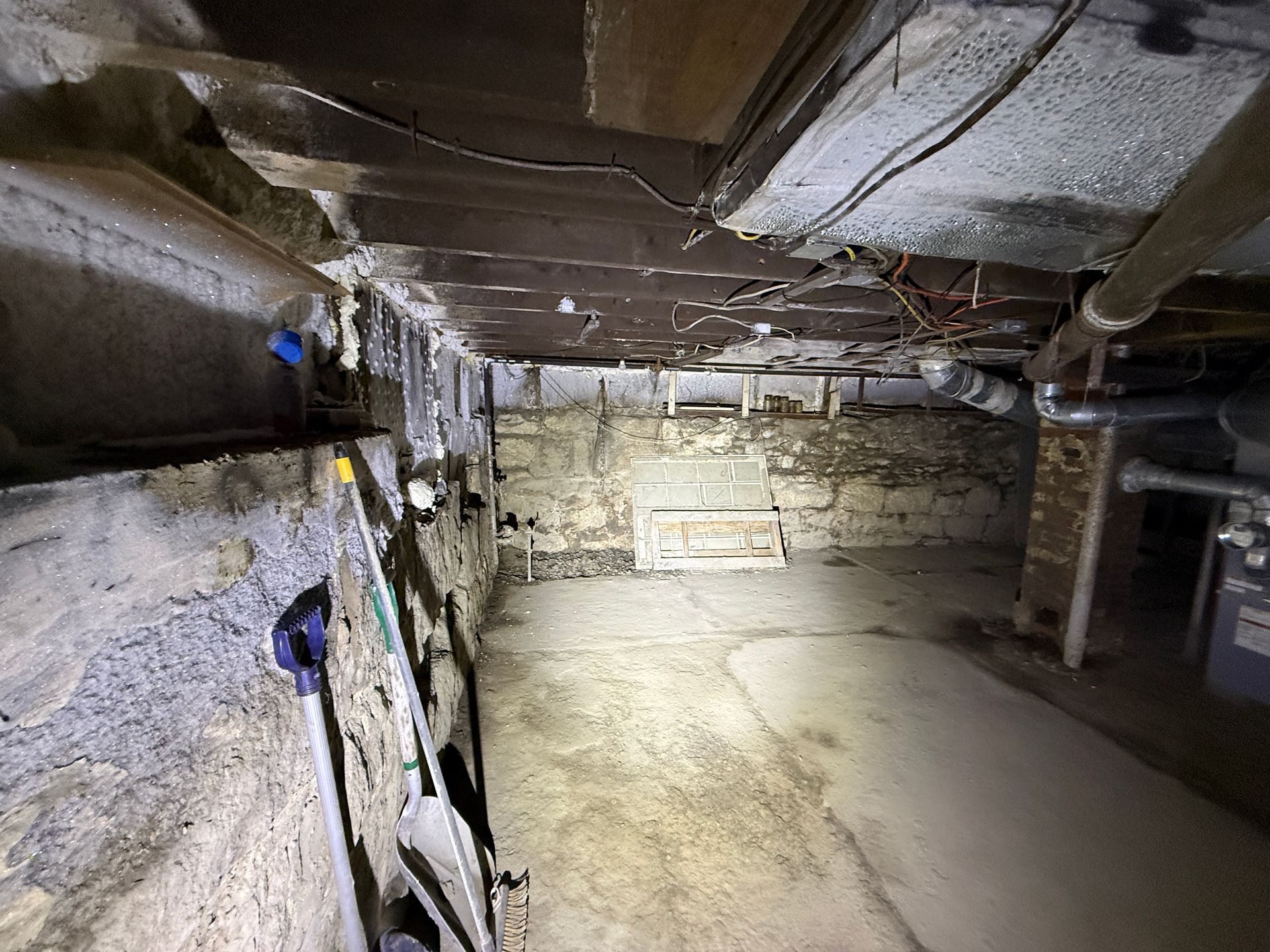 A basement with stone walls, wooden ceiling joists, and a concrete floor.
