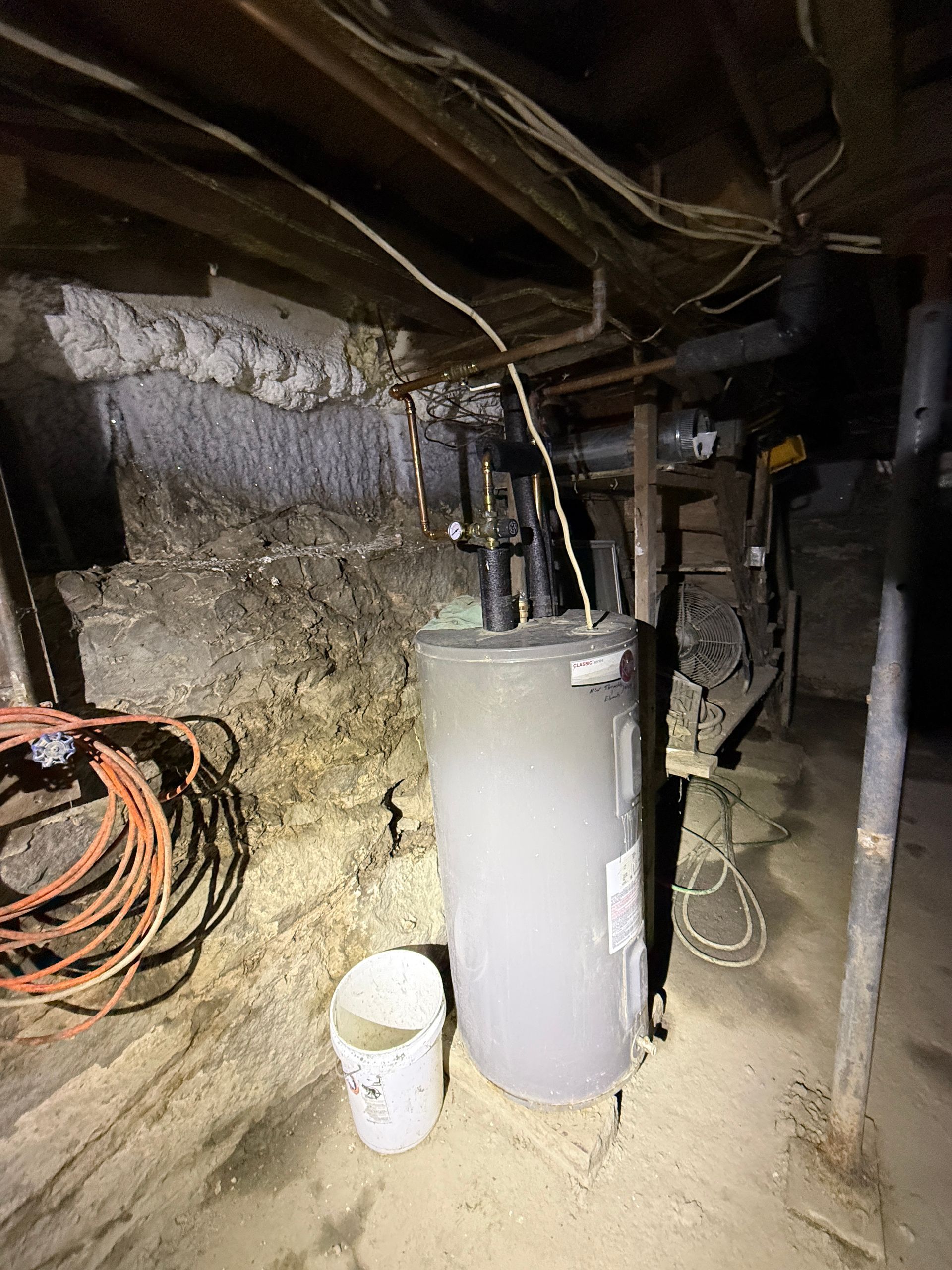 A gray hot water heater stands in a basement.