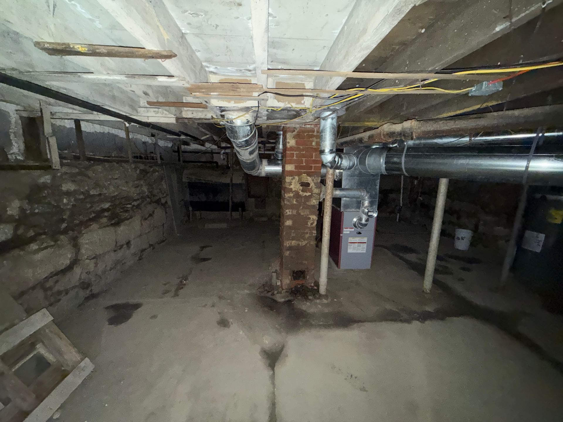 A basement with a concrete floor, a central brick chimney, exposed ceiling joists, and metal ductwork.