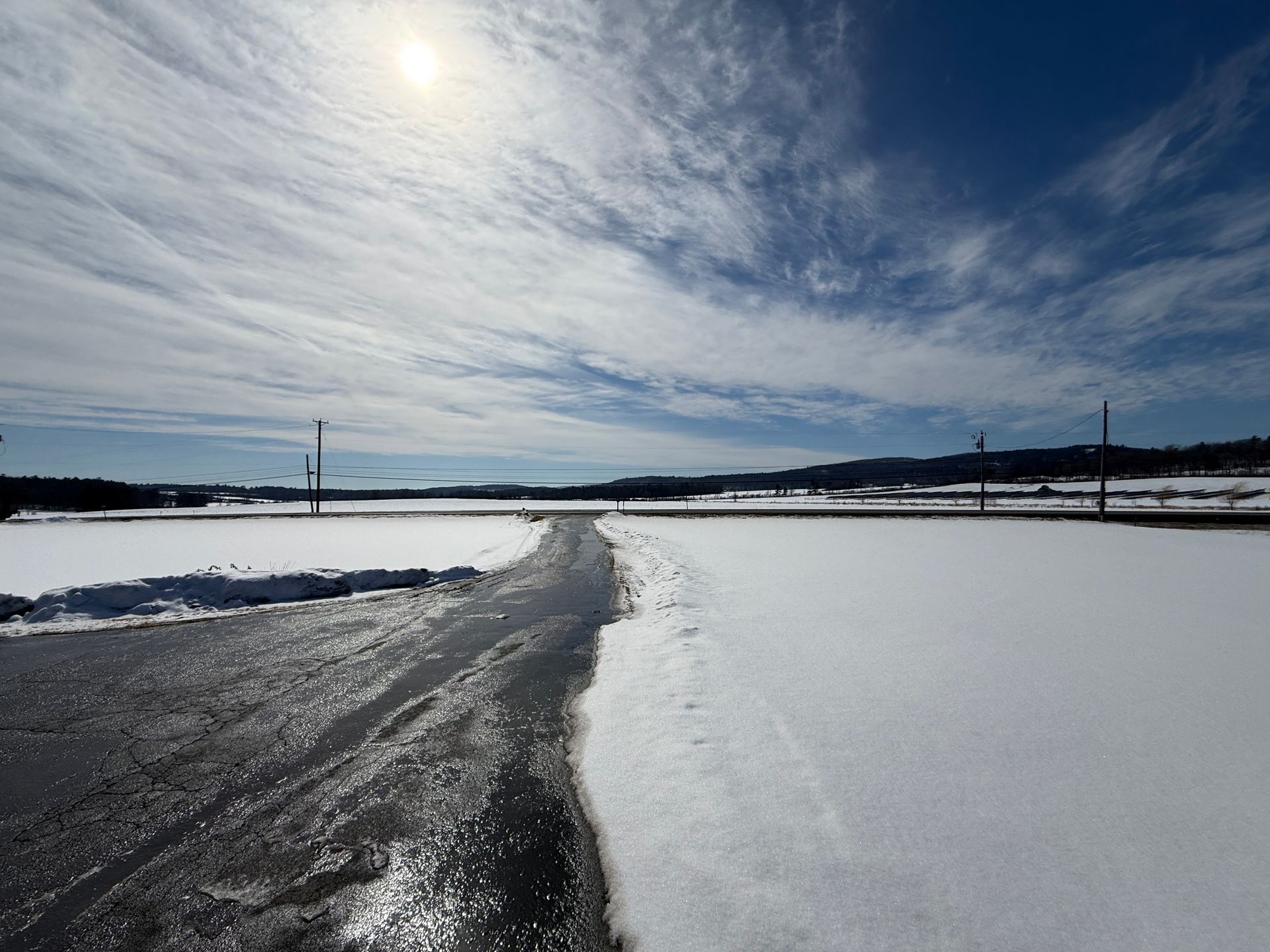 Snowy landscape with a road, bright sun, and blue sky with clouds.