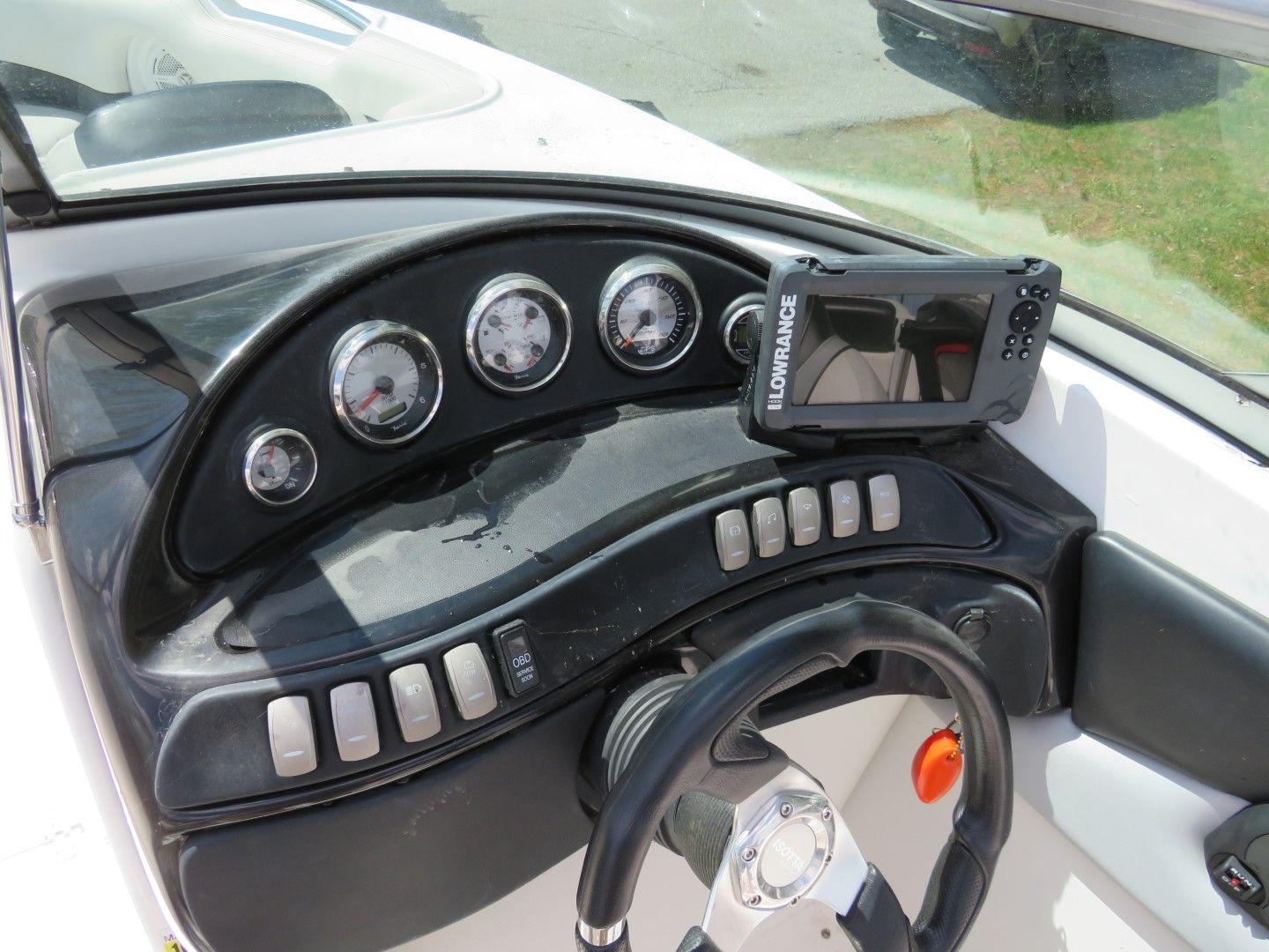 Boat dashboard with gauges, switches, steering wheel, and fish finder display.