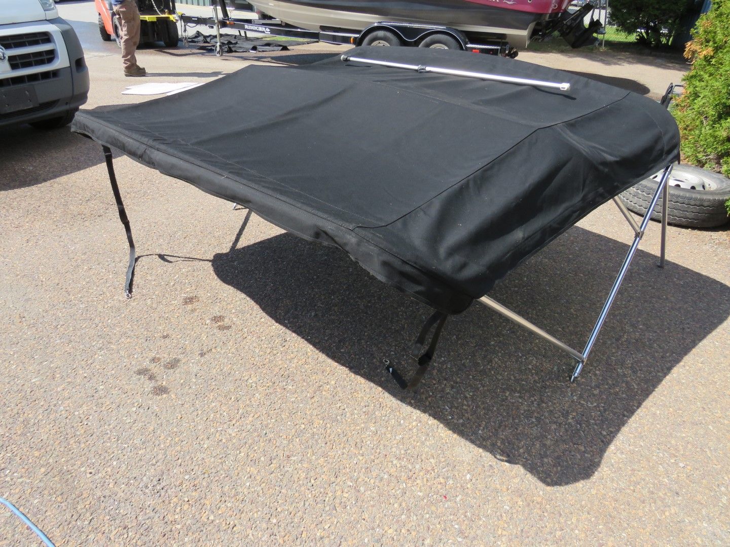 Black boat cover on a metal frame, set on gravel, with boat in background.