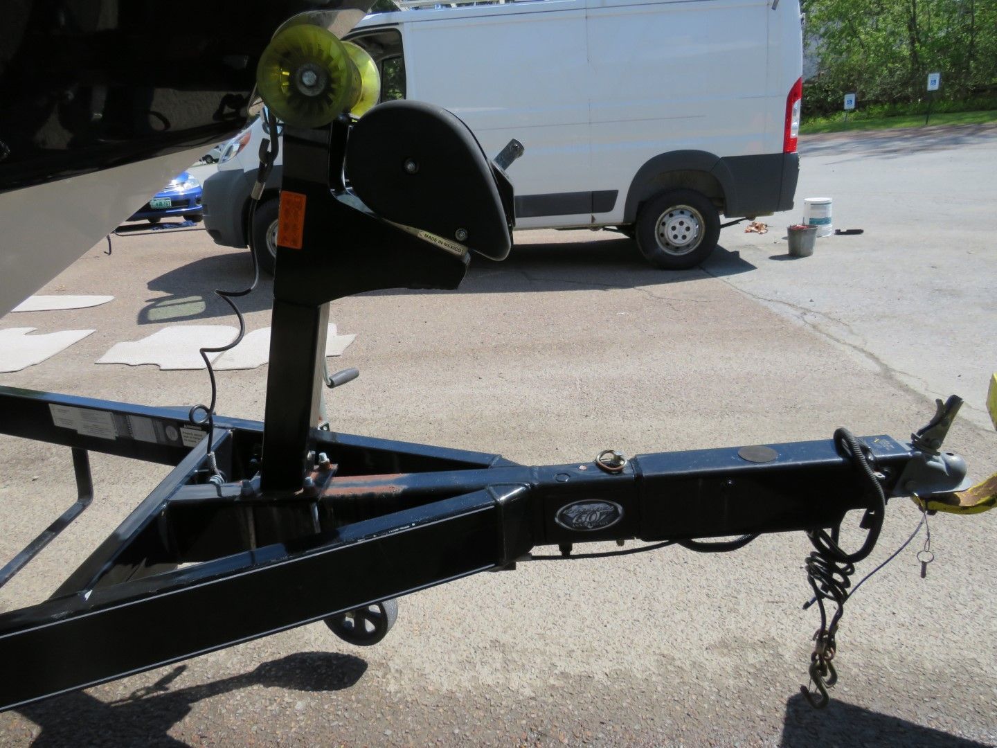 Black boat trailer with winch, hitched, parked on asphalt.
