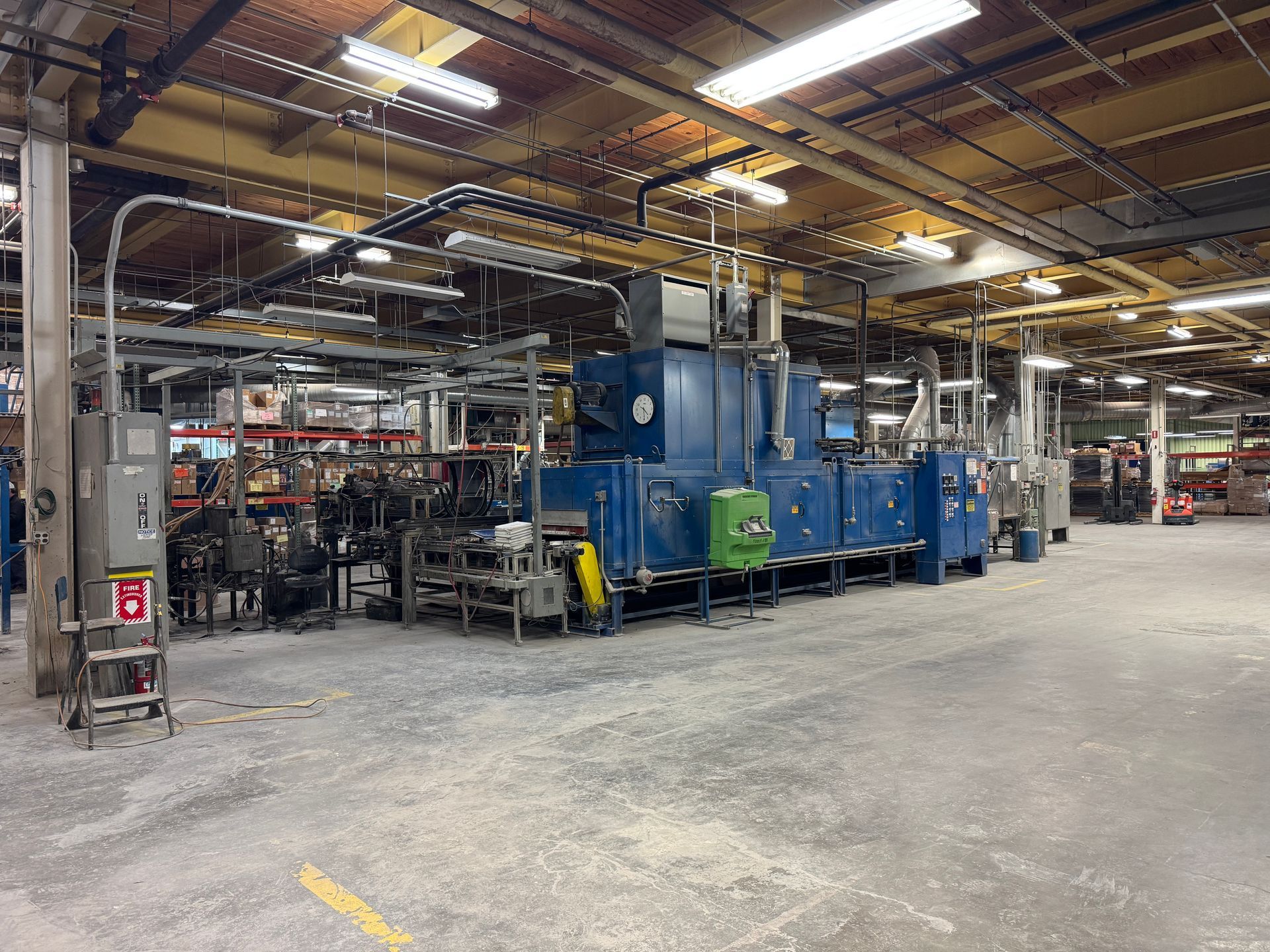 Industrial oven in a factory setting, blue, gray and green, with multiple pipes and a concrete floor.