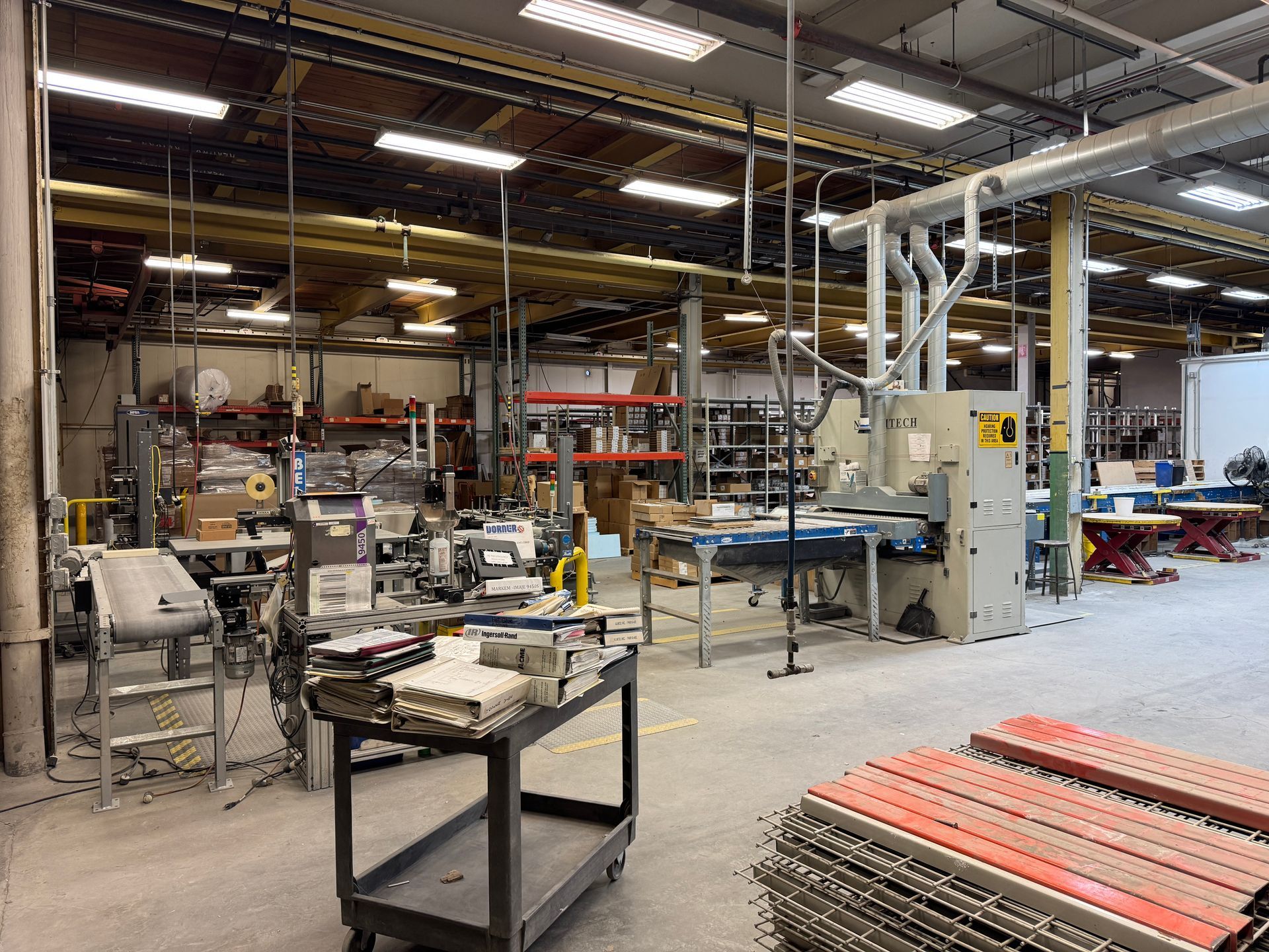 Interior factory shot with machinery, shelves of goods, and a cart, under industrial lighting.