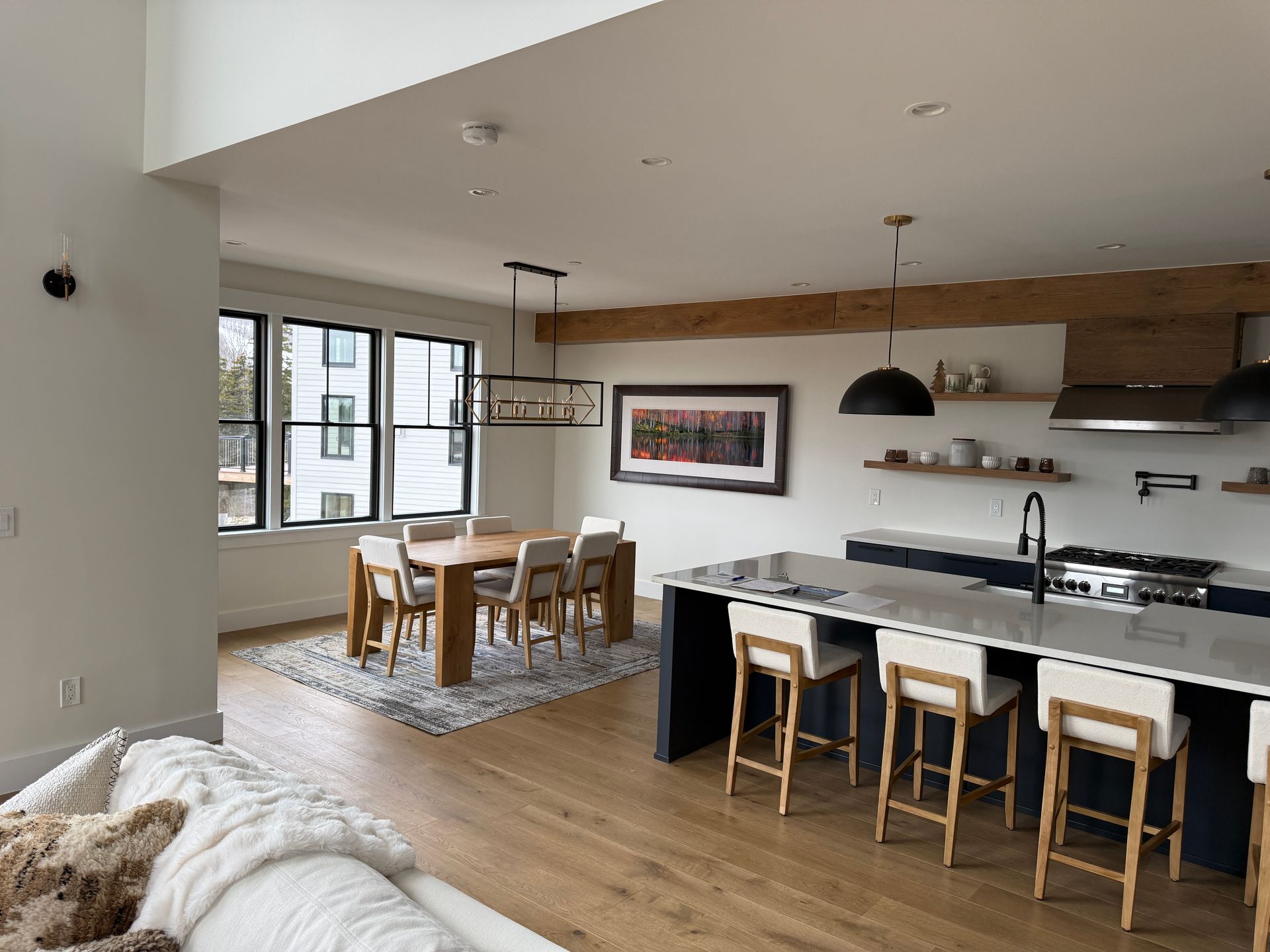 An open-concept kitchen and dining area featuring a dark blue island, light wood flooring, and neutral-toned decor.