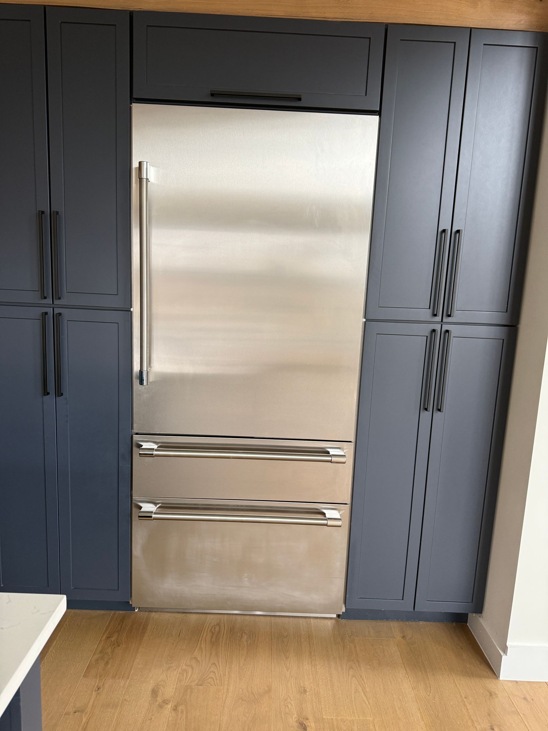 A stainless steel refrigerator built into dark blue cabinetry in a modern kitchen.