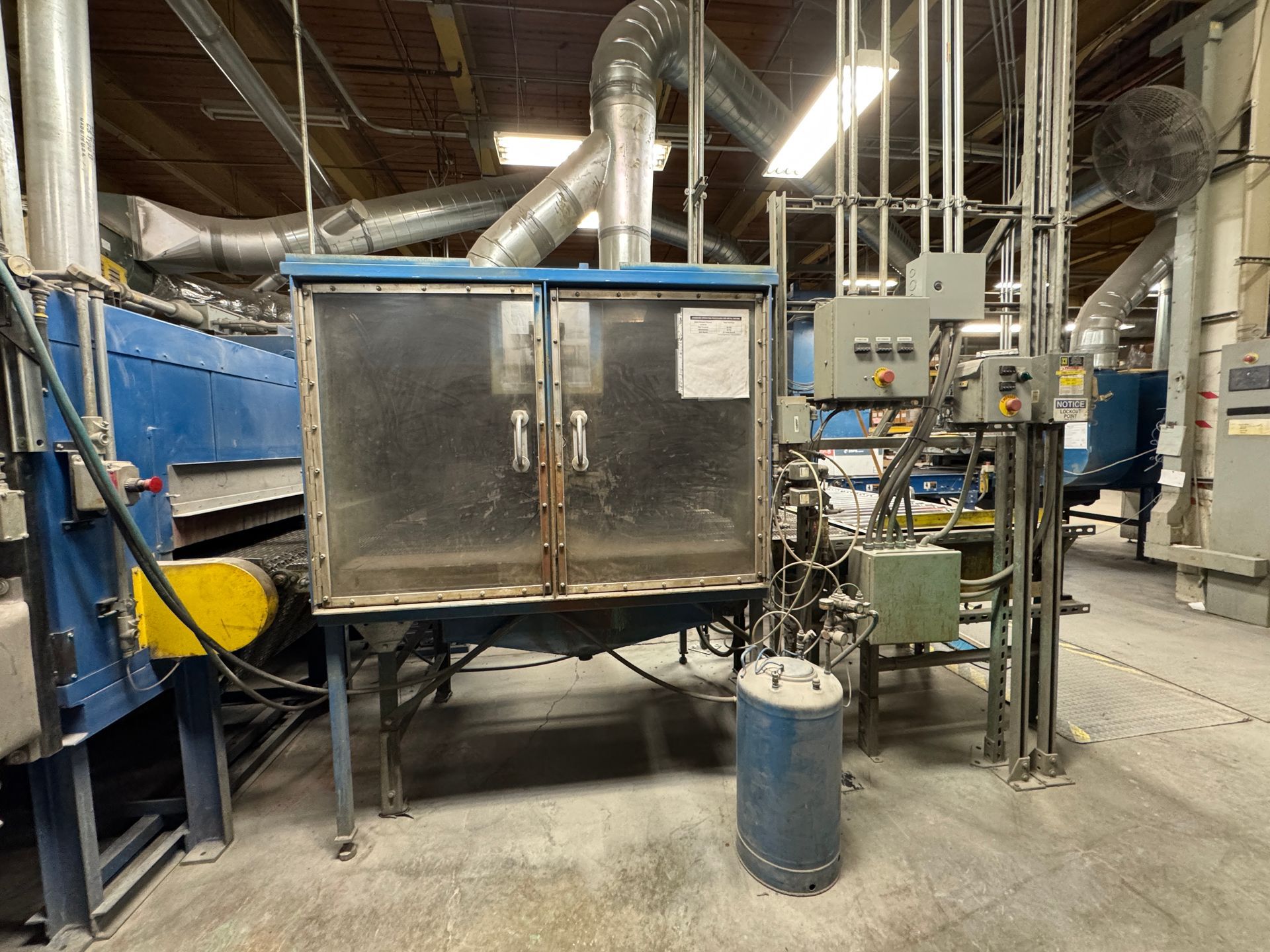 Industrial machinery with blue and silver components, vents, and a control panel in a factory setting.