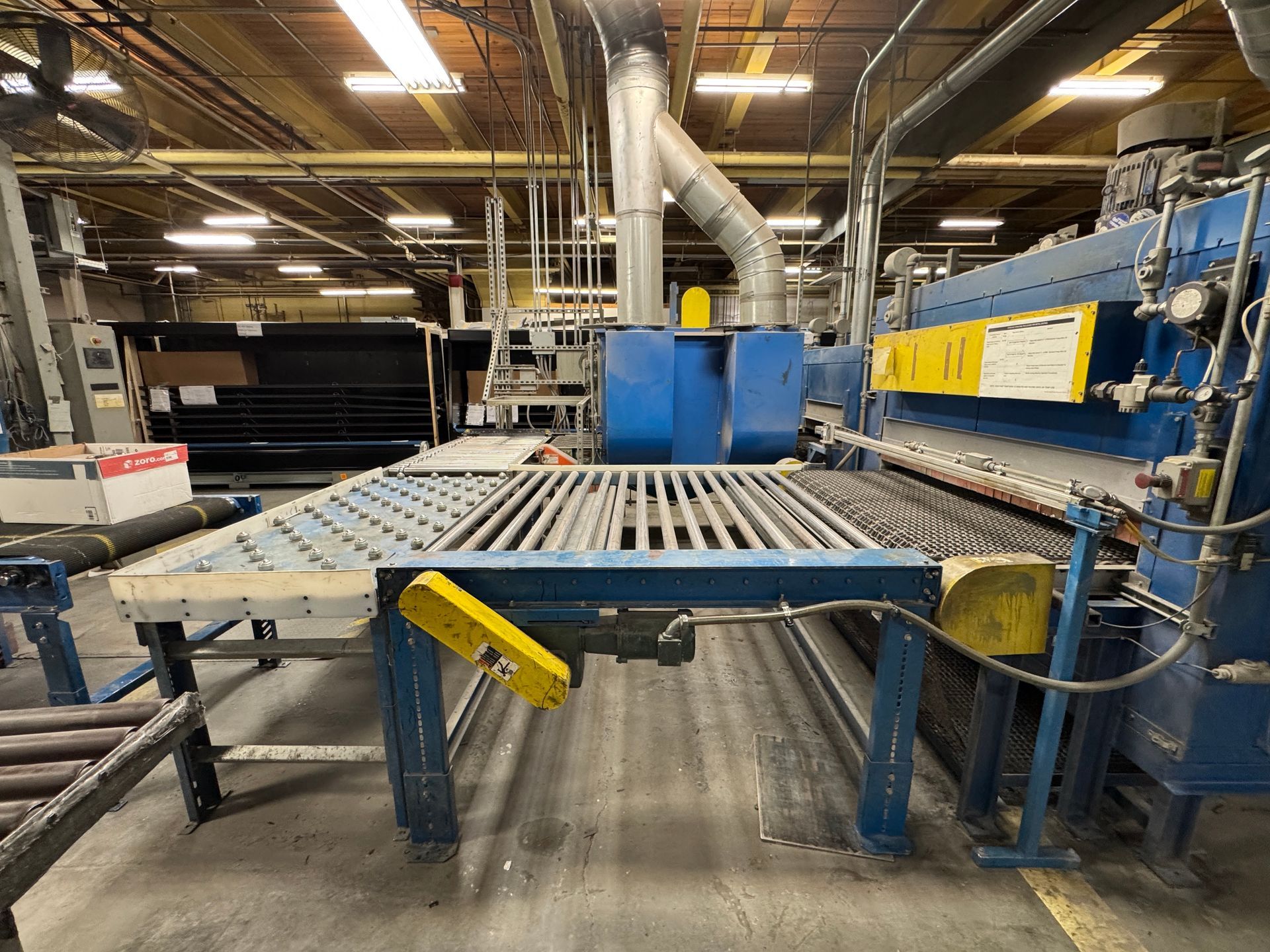 Industrial machinery in a factory setting, with a blue and gray metal frame and conveyor belt.