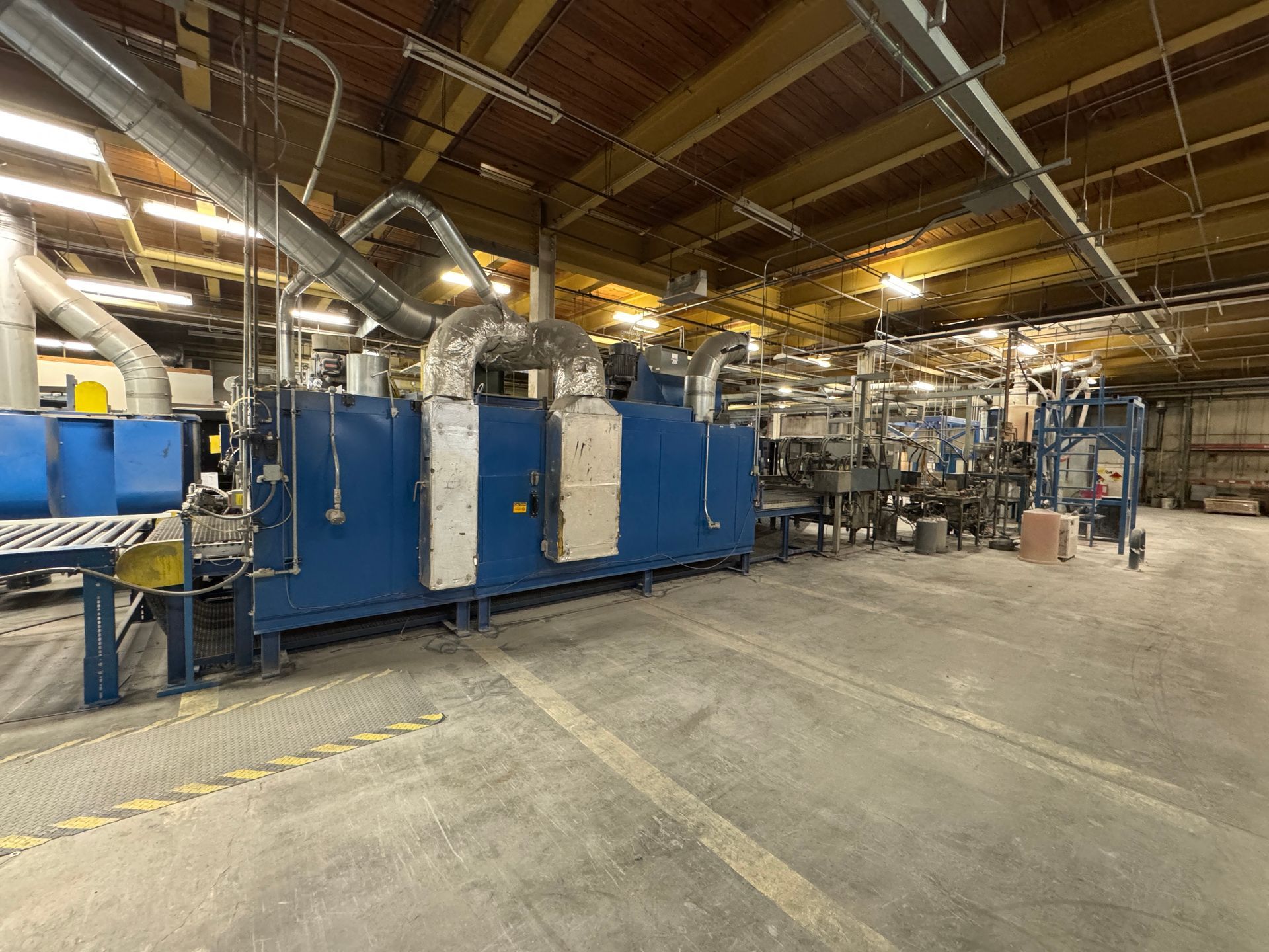 Blue industrial oven with connected metal pipes inside a warehouse.