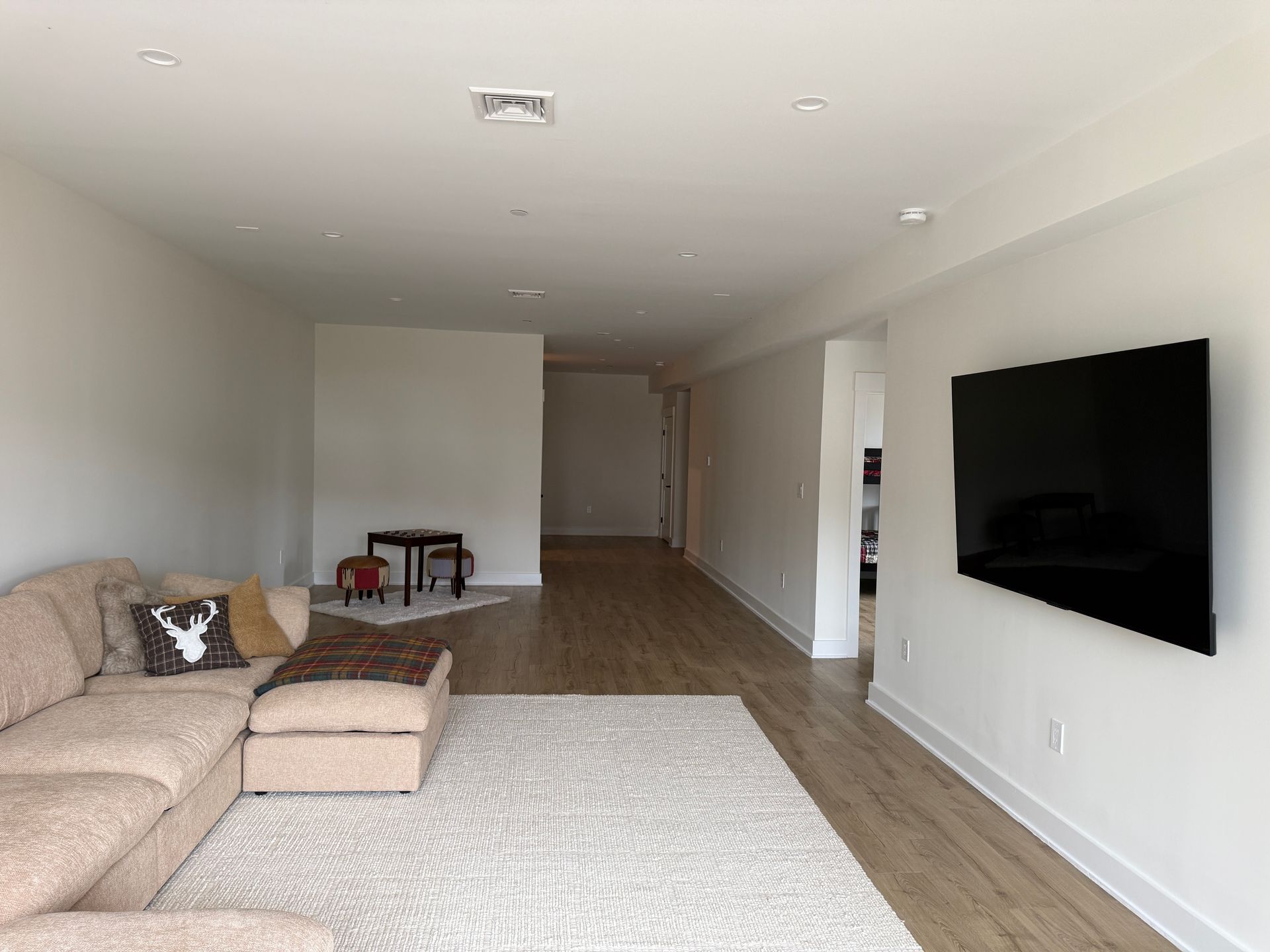 A beige sectional sofa on a light rug in a living room with a mounted television and hardwood floors.