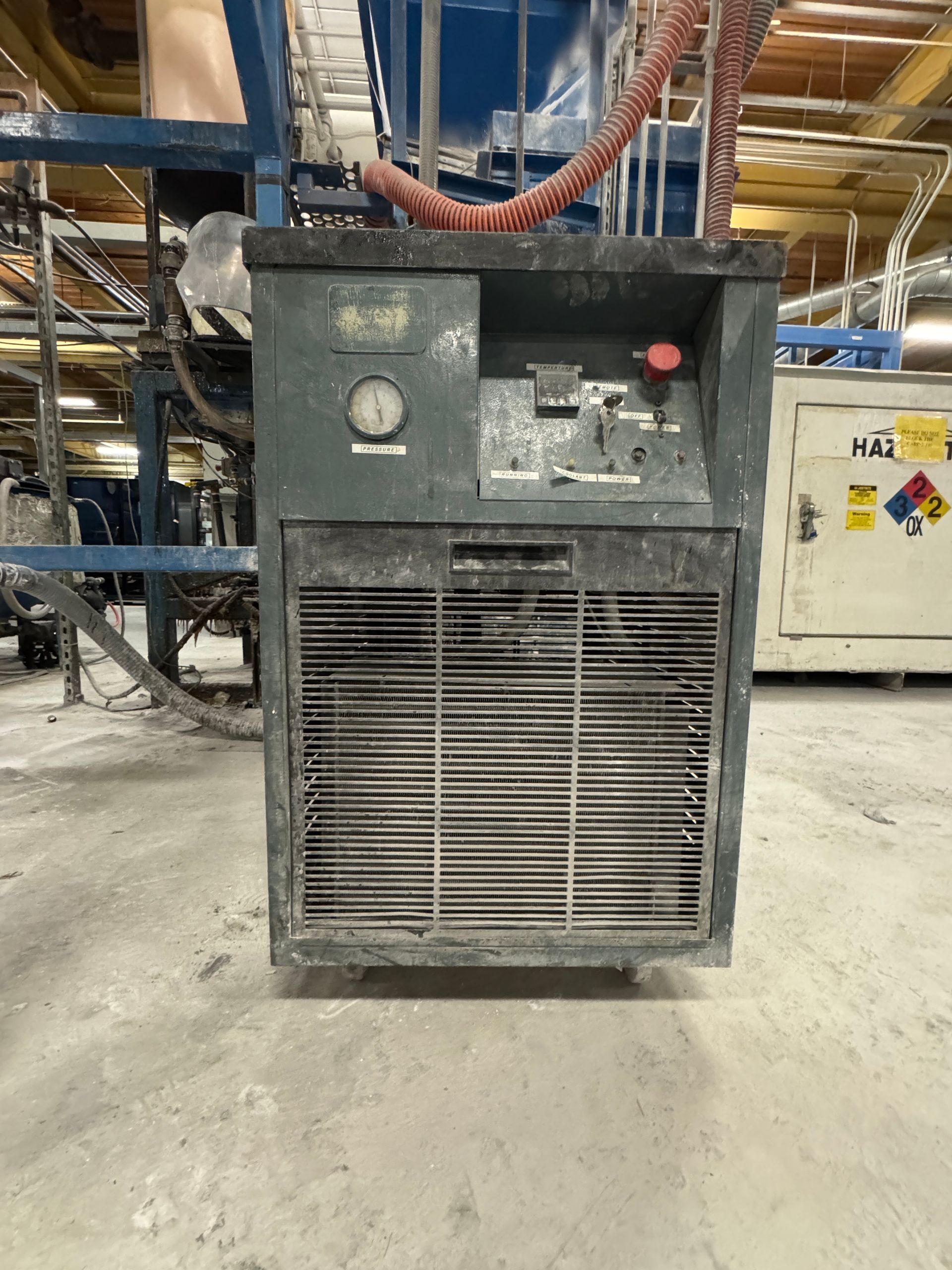 Industrial machine with a gray cabinet, pressure gauge, and ventilation grille, in a factory setting.