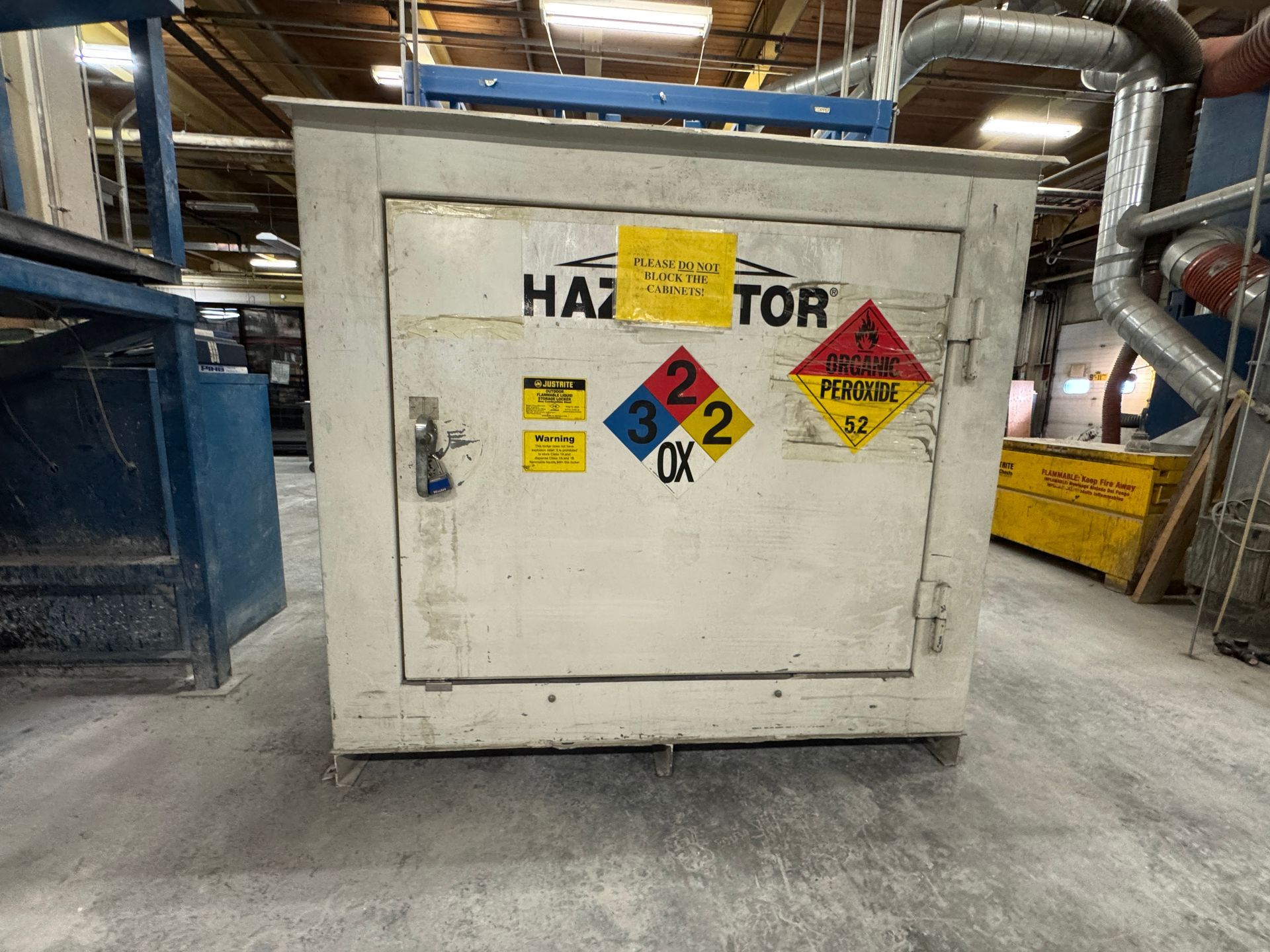 White hazmat storage cabinet with hazard labels in an industrial setting.